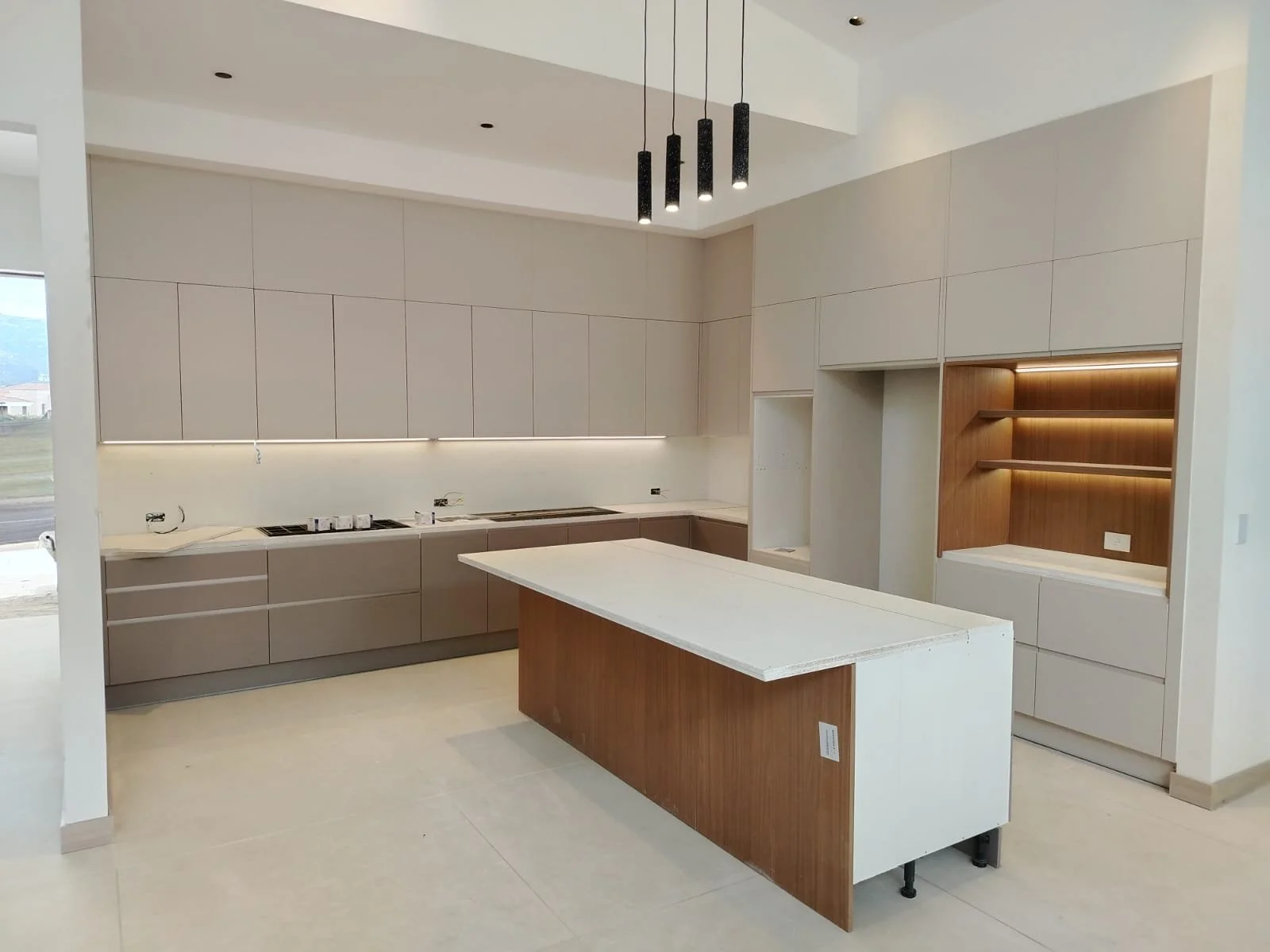Cocina moderna con isla central, gabinetes beige, estanterías con iluminación LED y diseño limpio y minimalista.
