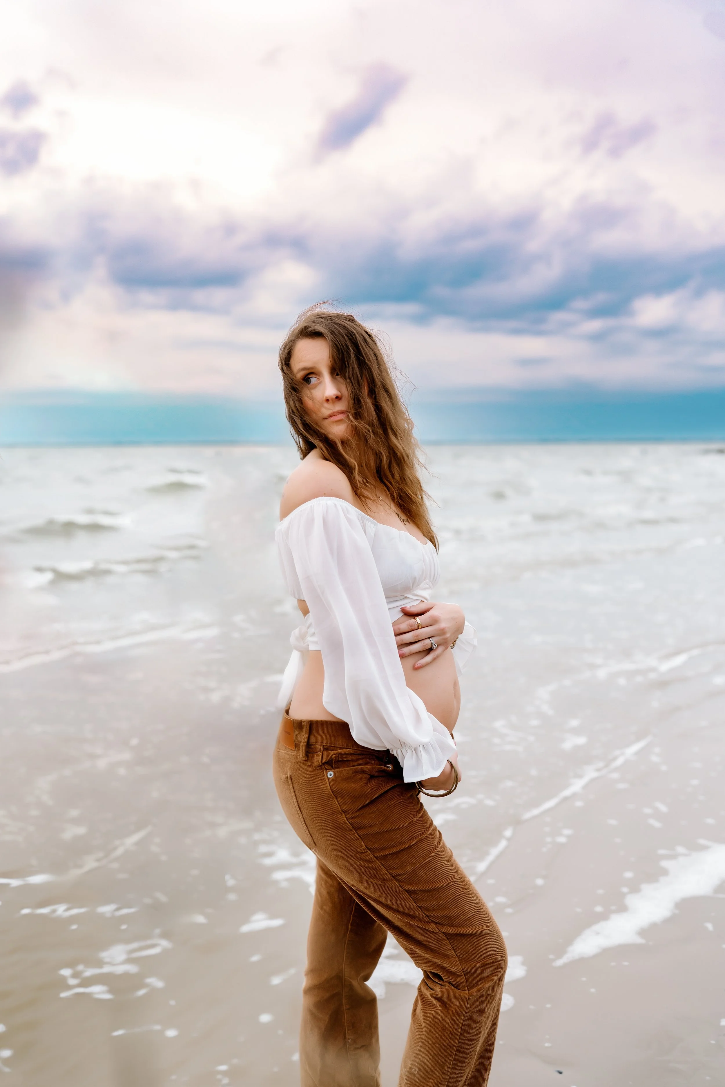 Pregnant mother embracing her baby bump during a beach maternity photography session in Galveston, TX