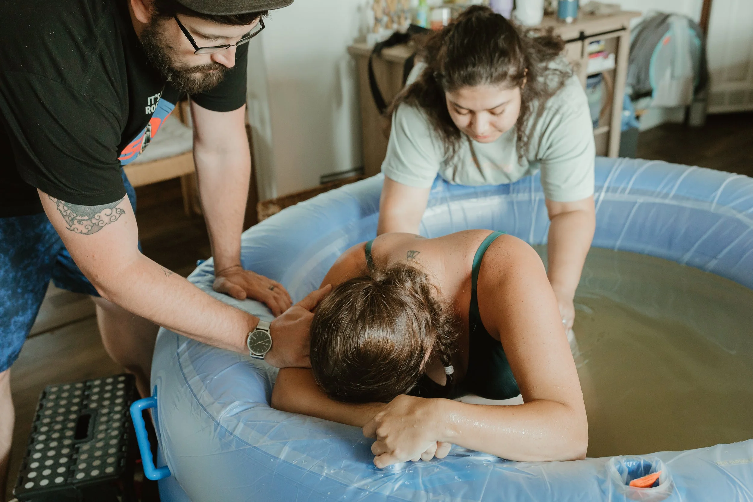 Mother laboring in a birth pool with support from her partner and doula during a water birth in The Woodlands, TX