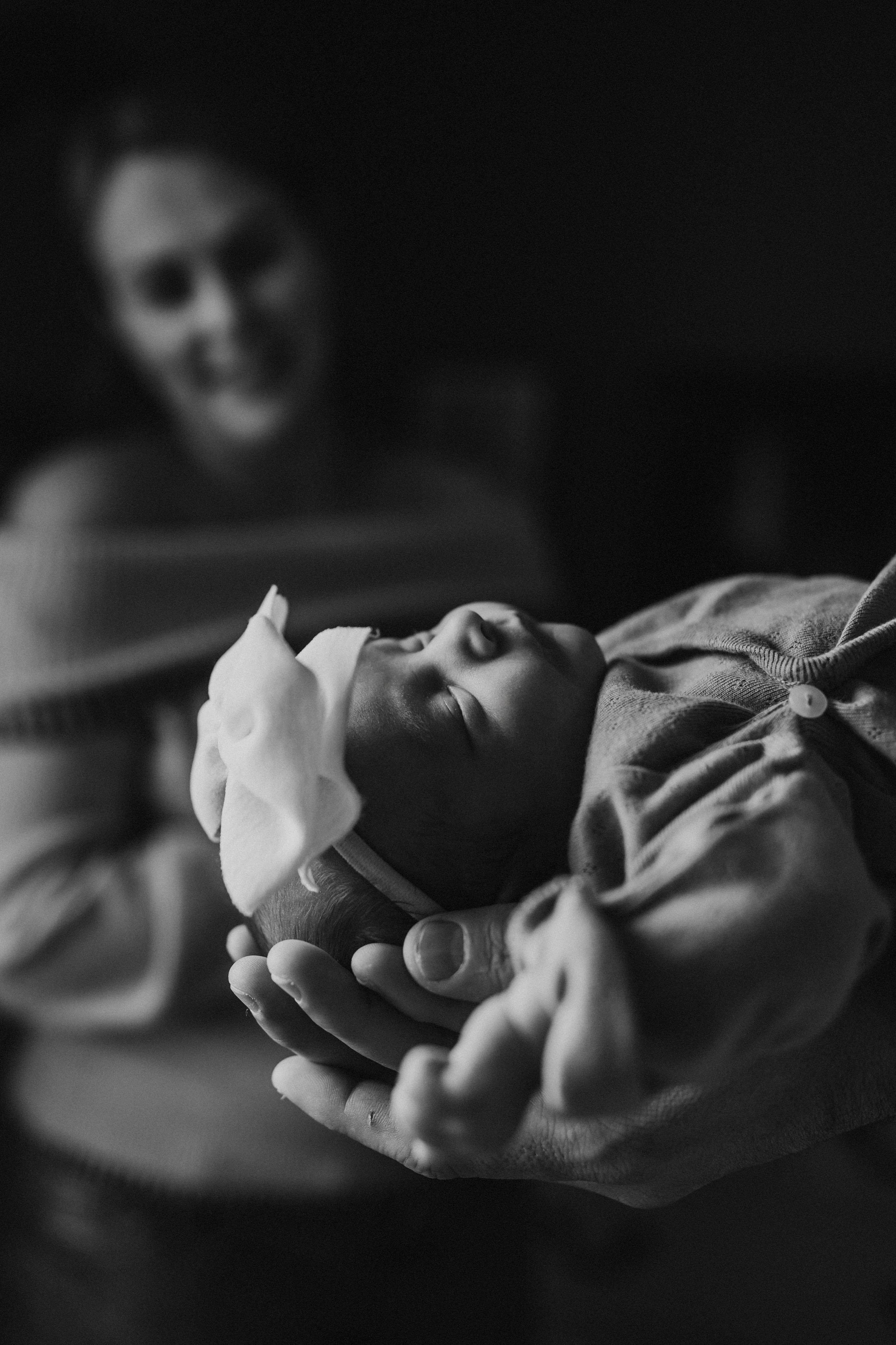 Black and white photograph of a newborn baby being gently held