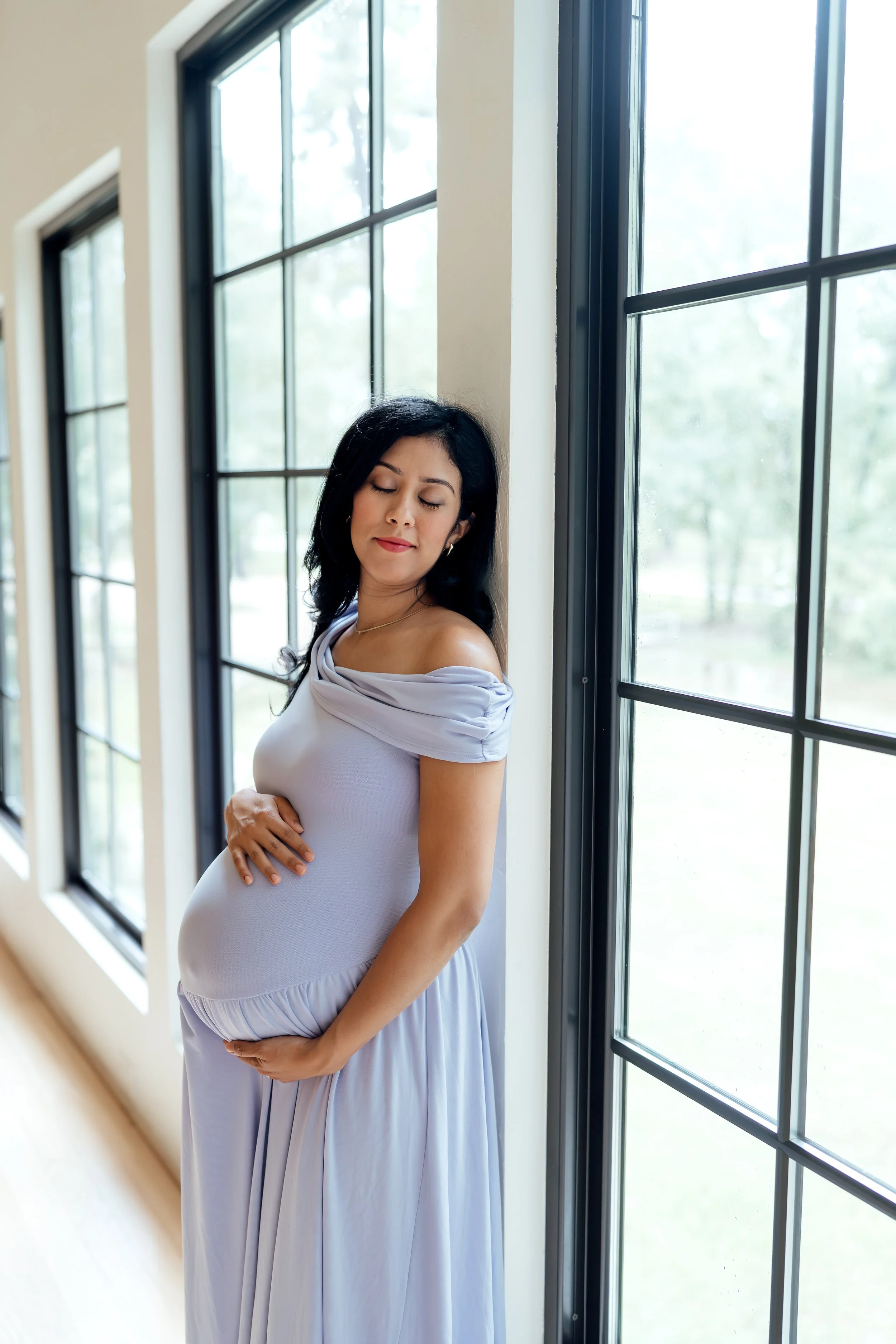 Pregnant mother posing by a window during a natural light maternity photography session in The Woodlands, TX