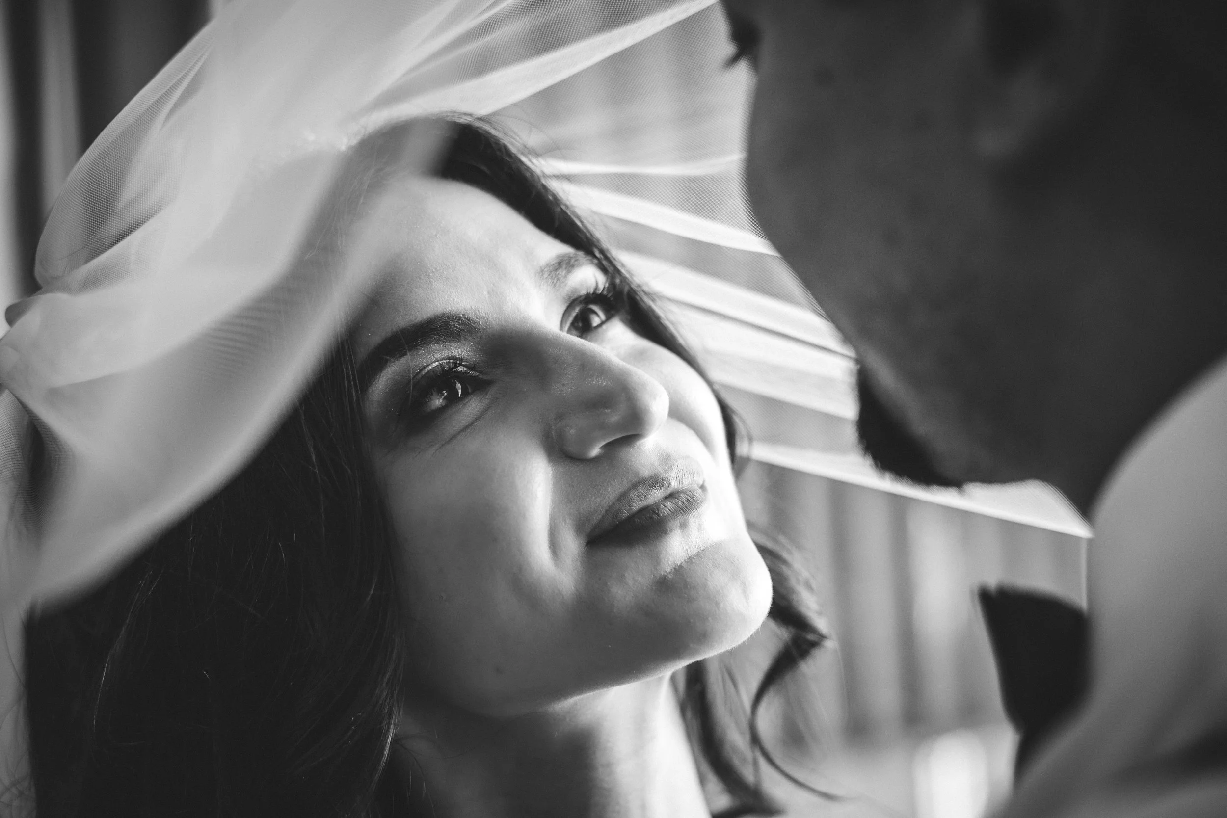 A woman with a bridal veil looking into a man’s eyes, close-up black and white photo.