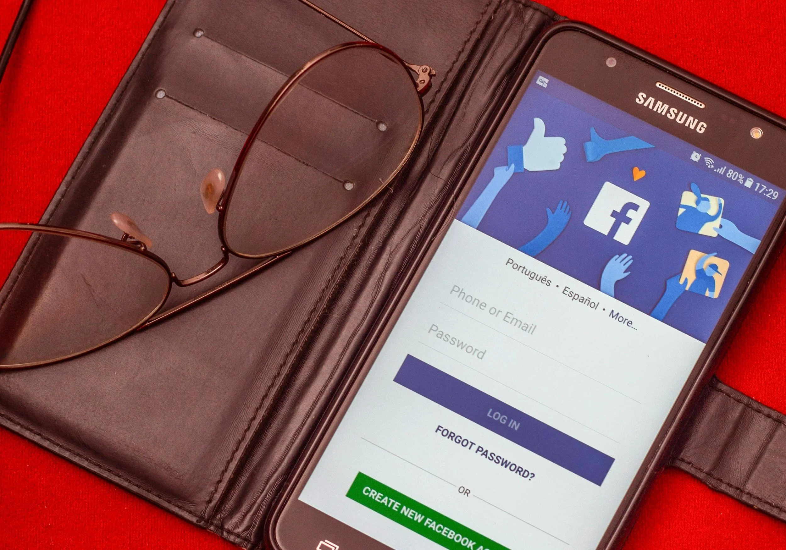 Smartphone displaying Facebook login page, placed in a leather case with reading glasses.