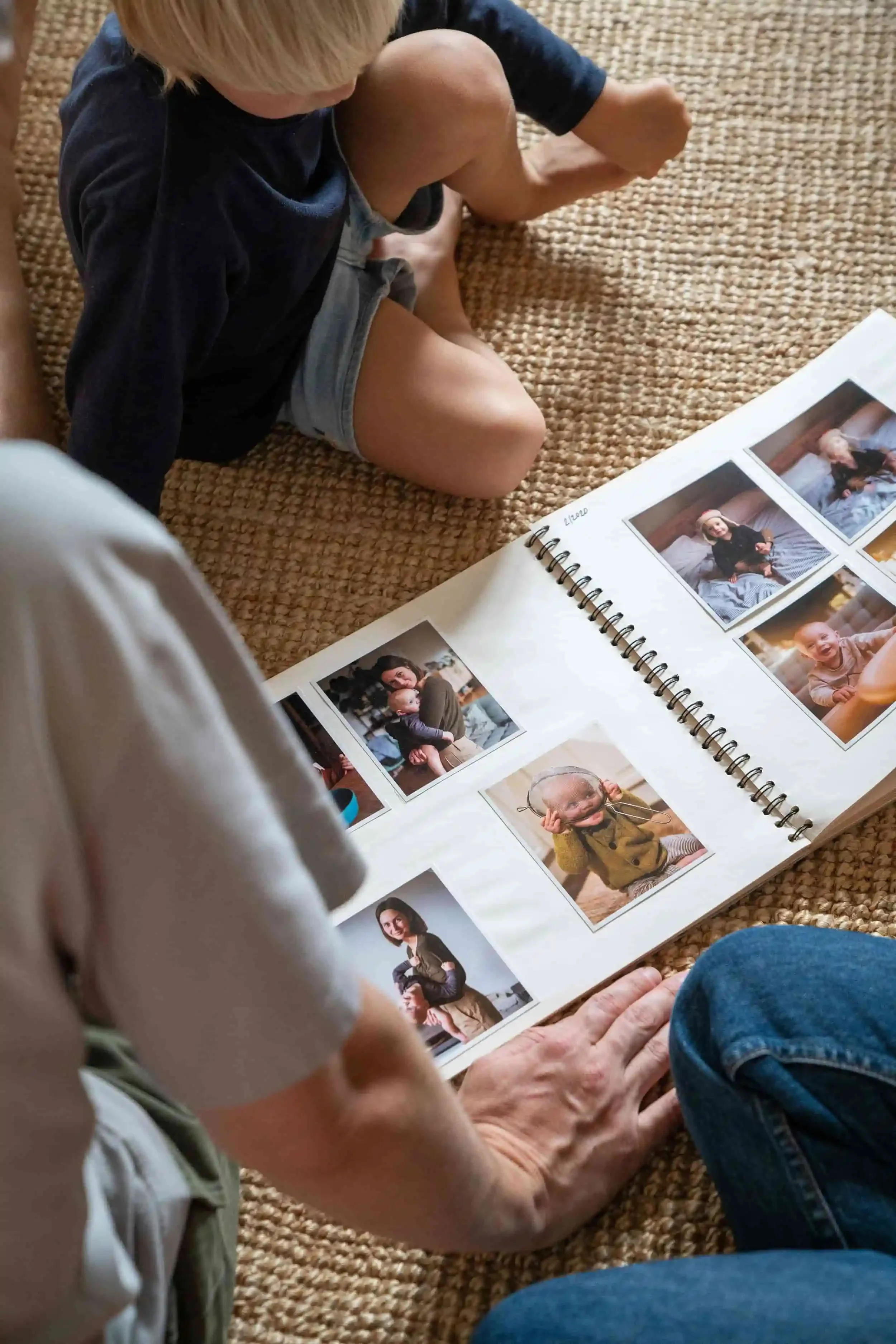 A child and an adult sit on a rug looking at a photo album filled with family pictures.
