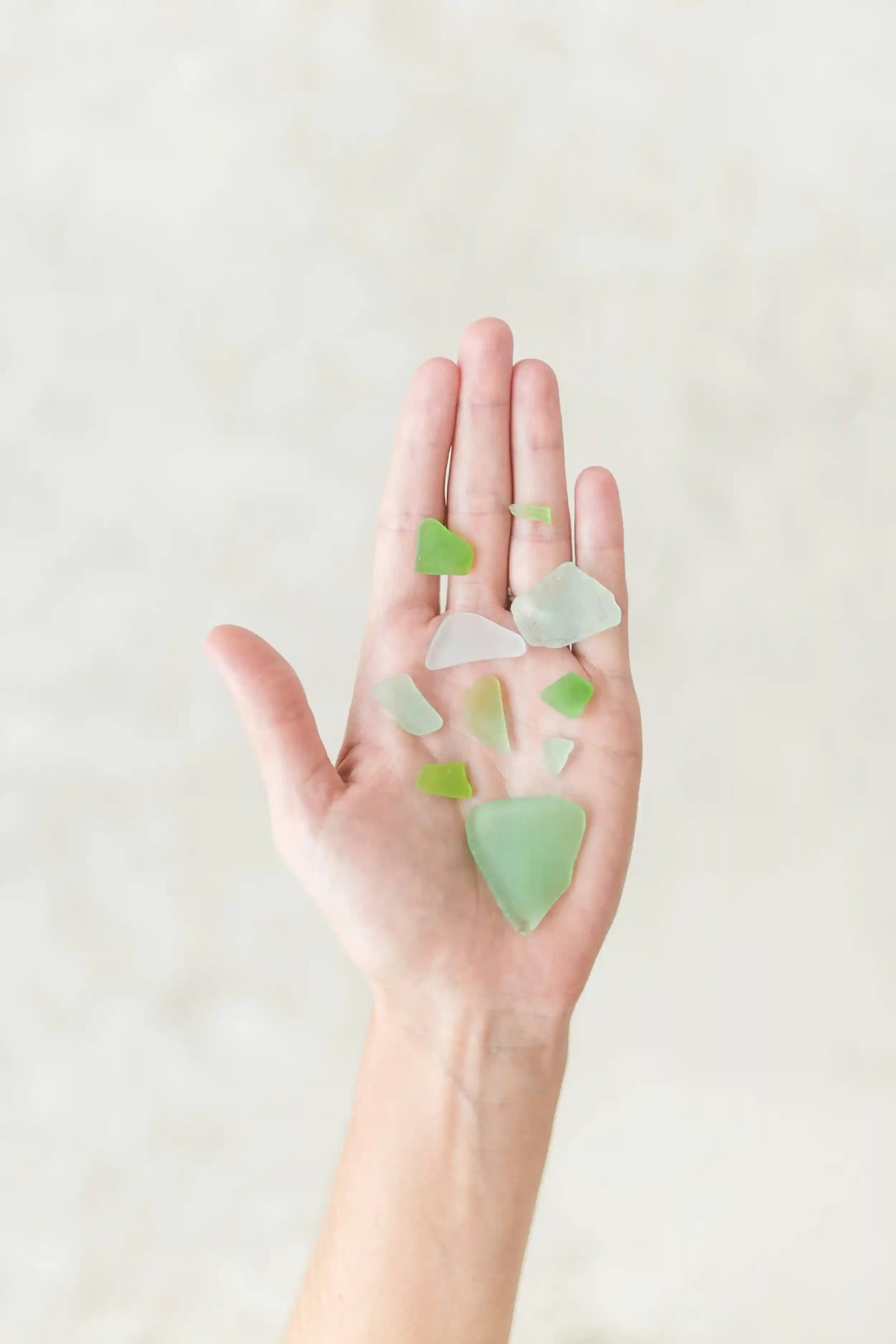 An open hand holding several pieces of smooth green and clear sea glass against a light, blurred background.