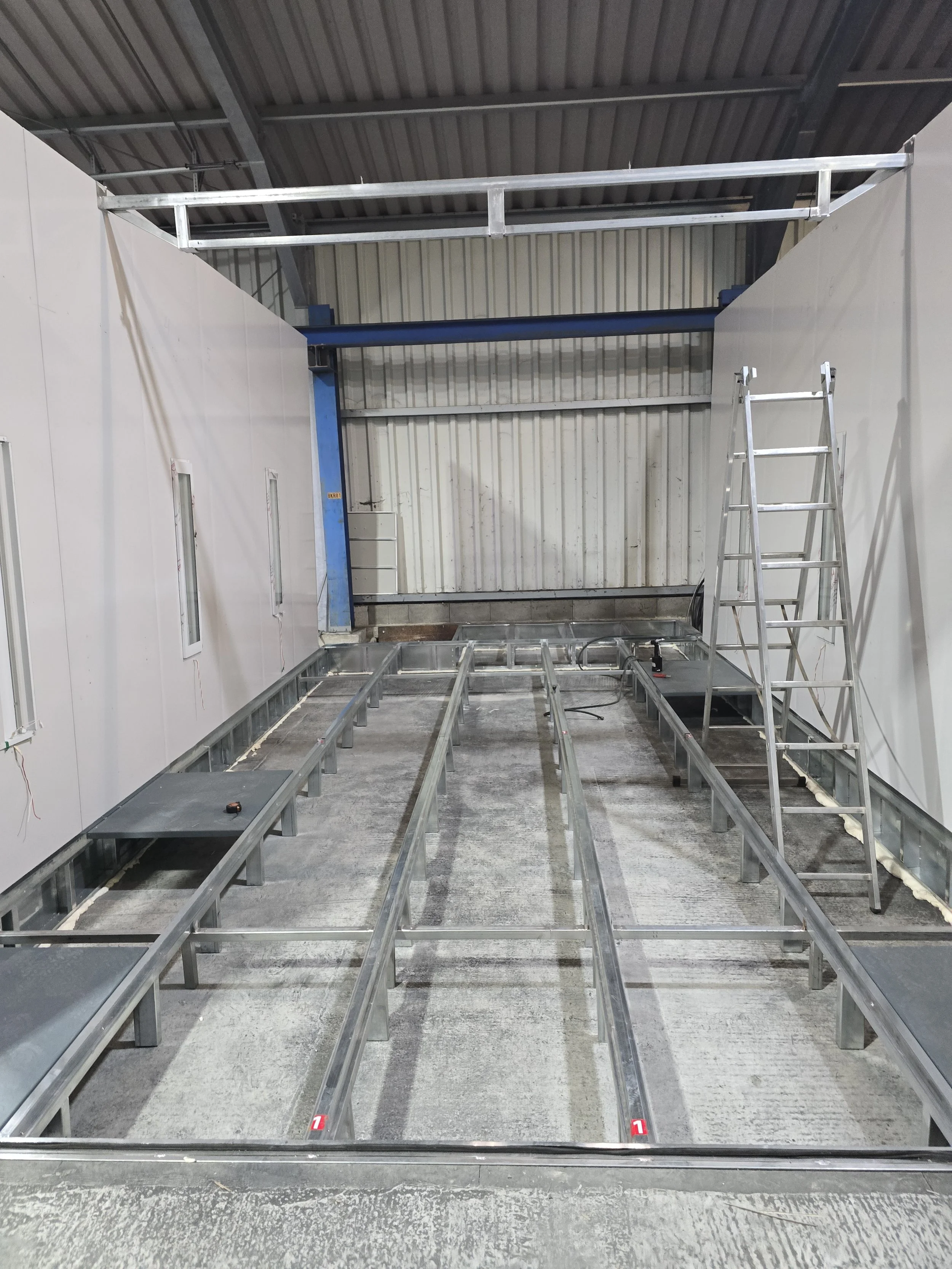 Baufahrzeug mit Metallrahmen und Leiter in einer Werkshalle, im Aufbau befindlich.