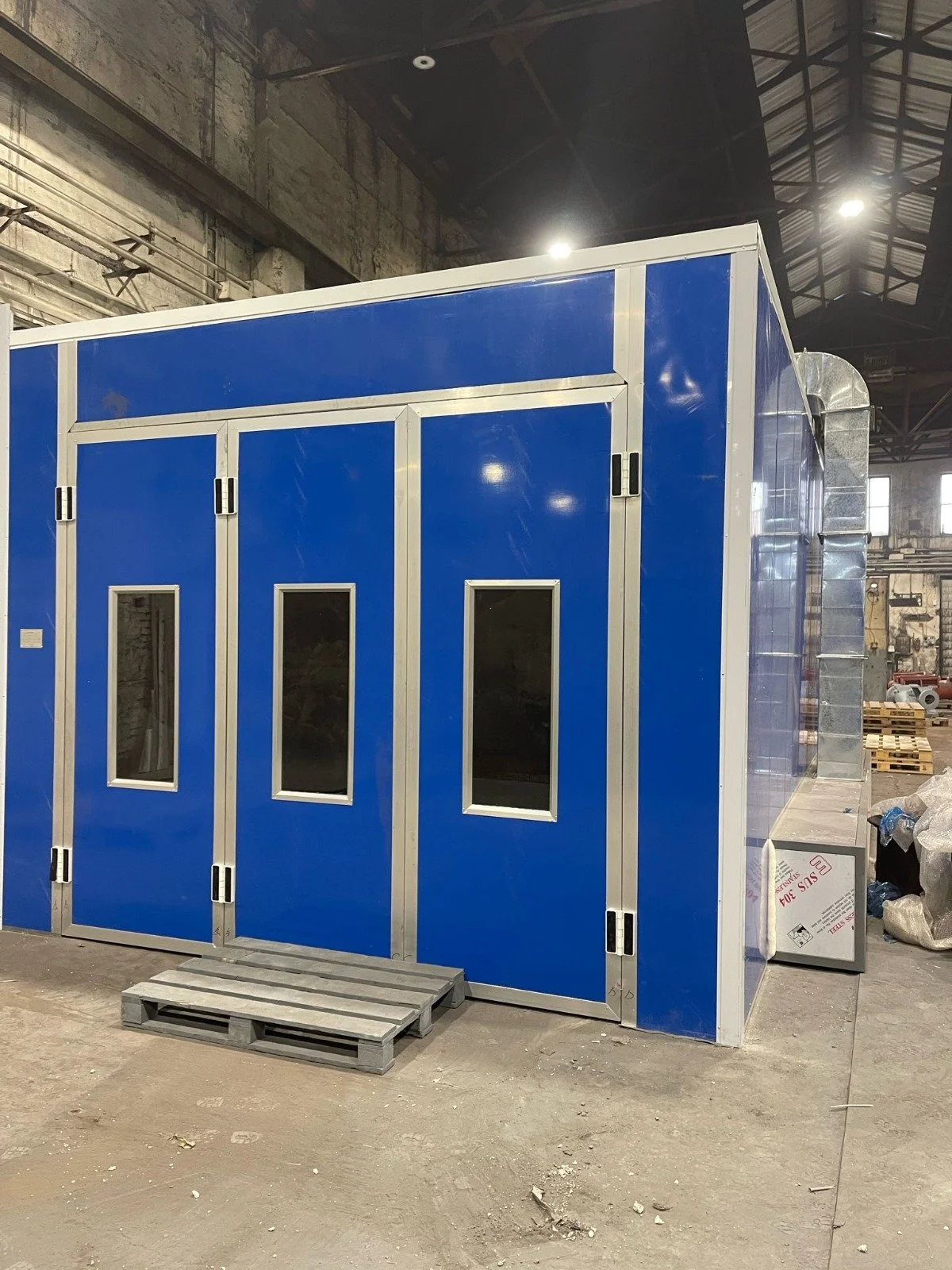 Ein blauber Kasten mit vier Türen mit kleinen Fenster in einer Industriehalle.