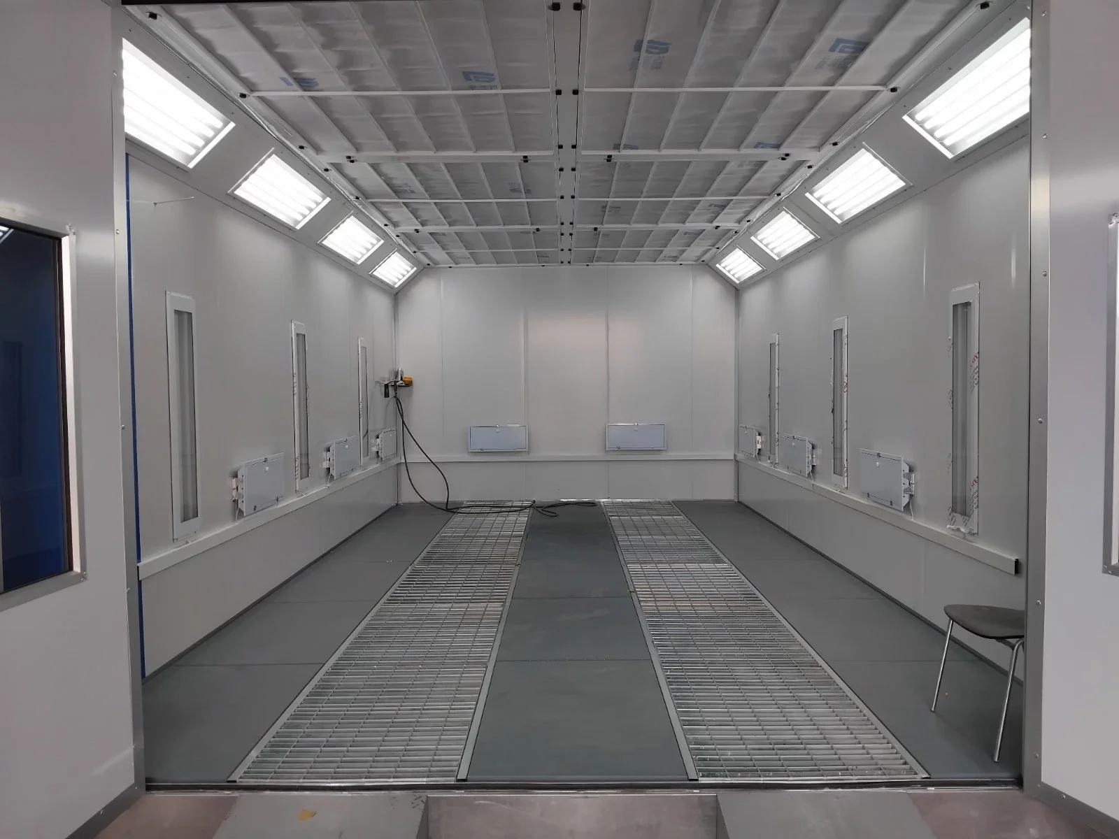 Leeres, weißes Isolierraum mit Lüftungsschlitzen an der Decke und mehreren Kabelanschlüssen an den Wänden.