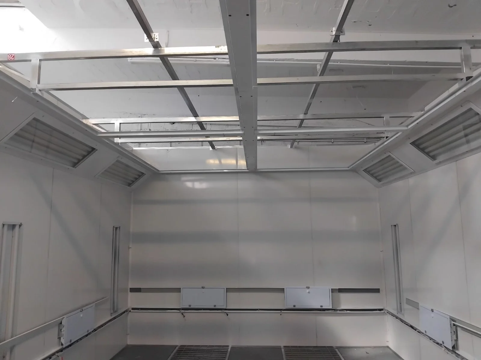 Leere industrielle Kühlzelle mit weißen Wänden, Lüftungssystemen und Gitterboden.