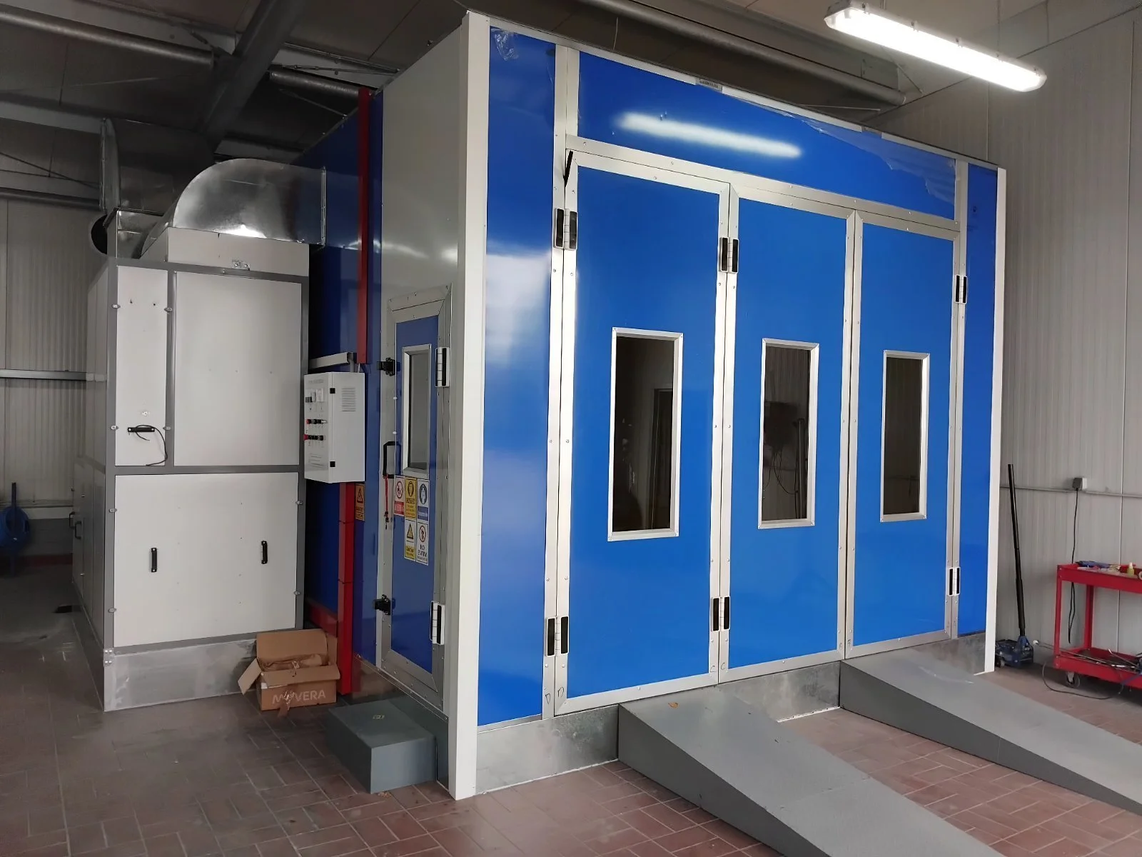 Reinraum mit blauer Isolierkabine, Kontrollfenstern und Metallrampe, in einem industriellen Umfeld.