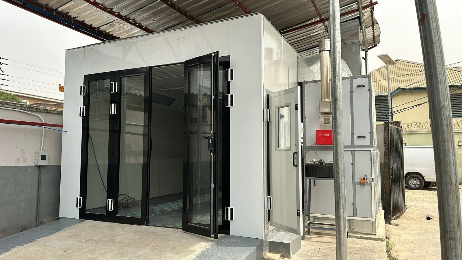 Ein kleiner, moderner Schrein mit Glas- und Metalltüren, installierte technische Geräte und ein Wasserhahn im Außenbereich.