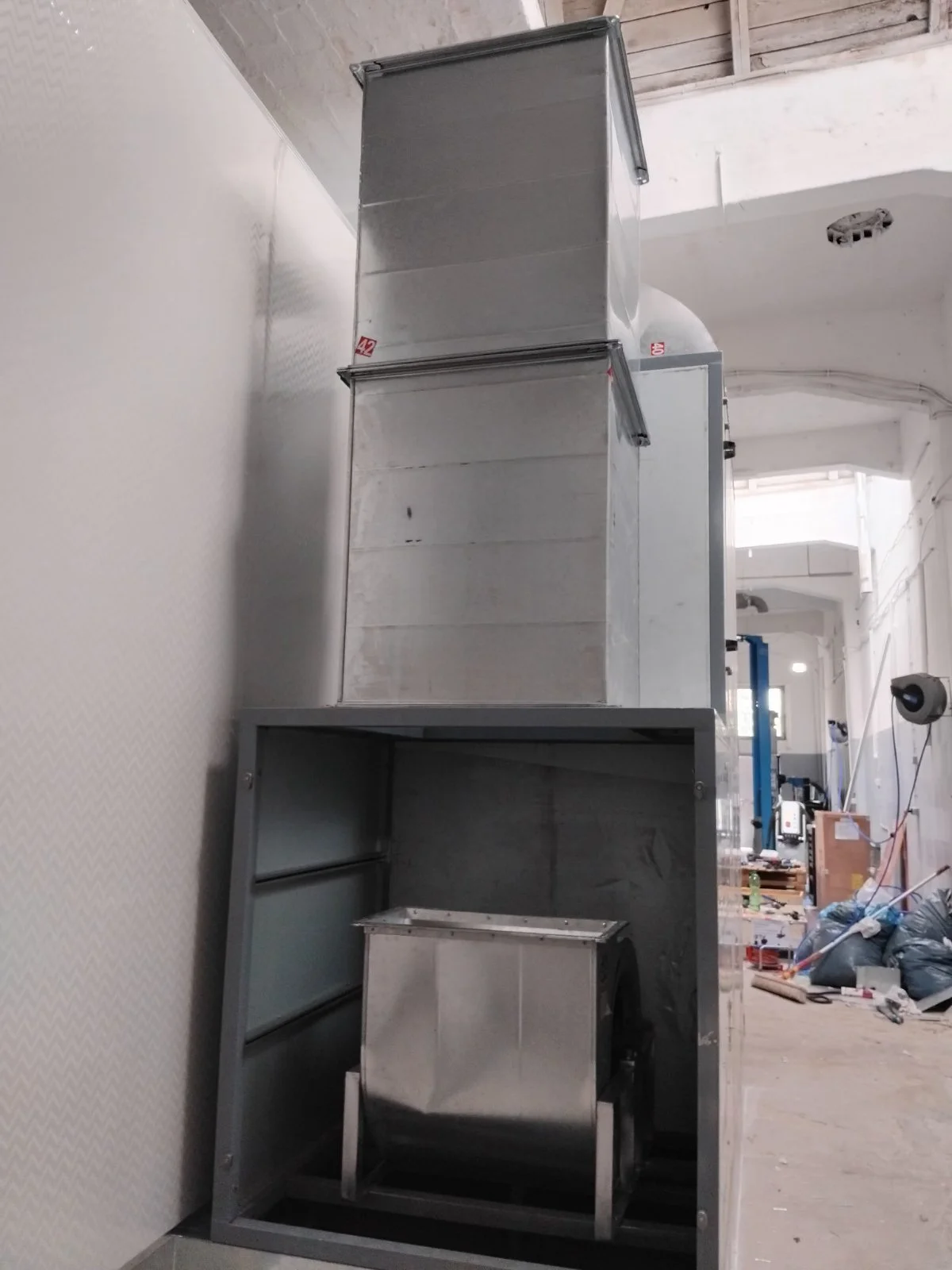 Mehrere große metallic-Boxen und ein kleines metal-Container in einem Raum mit offener Decke, im Hintergrund sind Baustellenmaterialien und Geräte sichtbar.