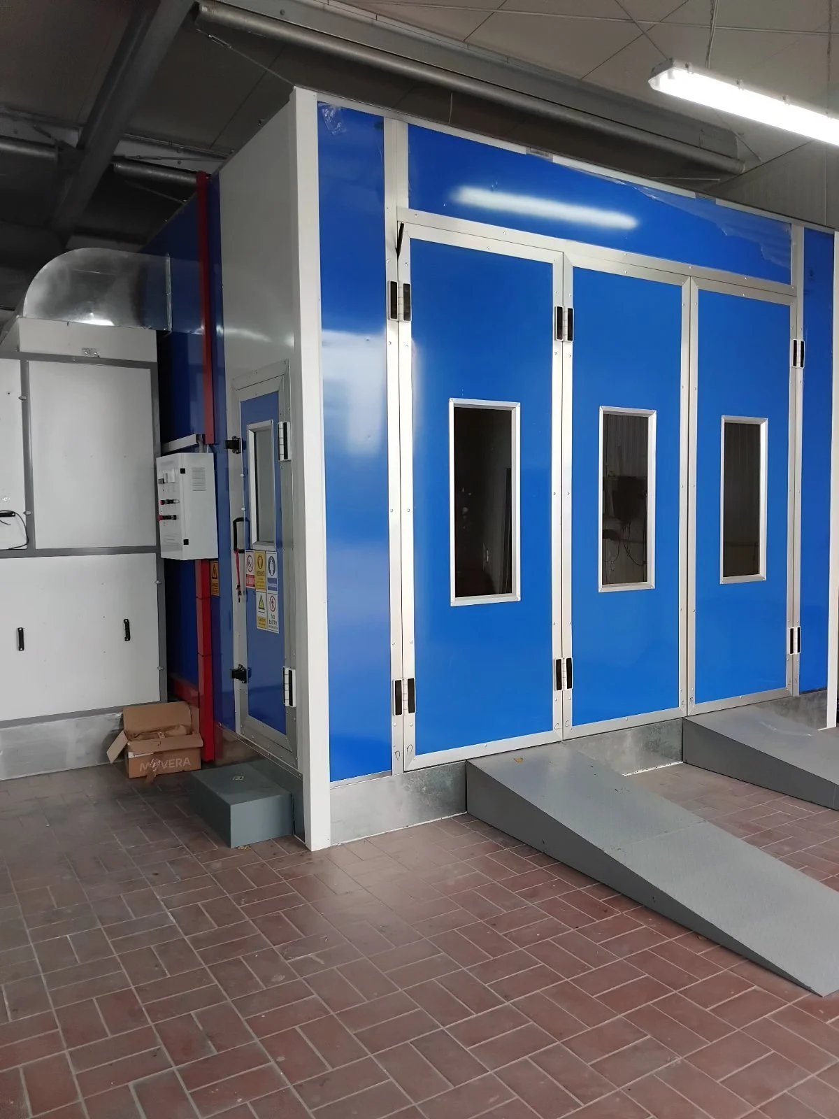 Ein blauer und weißer Kontrollraum mit drei Fenstern, Zugangstreppe und Steuerungselementen, vermutlich in einer Industriehalle.