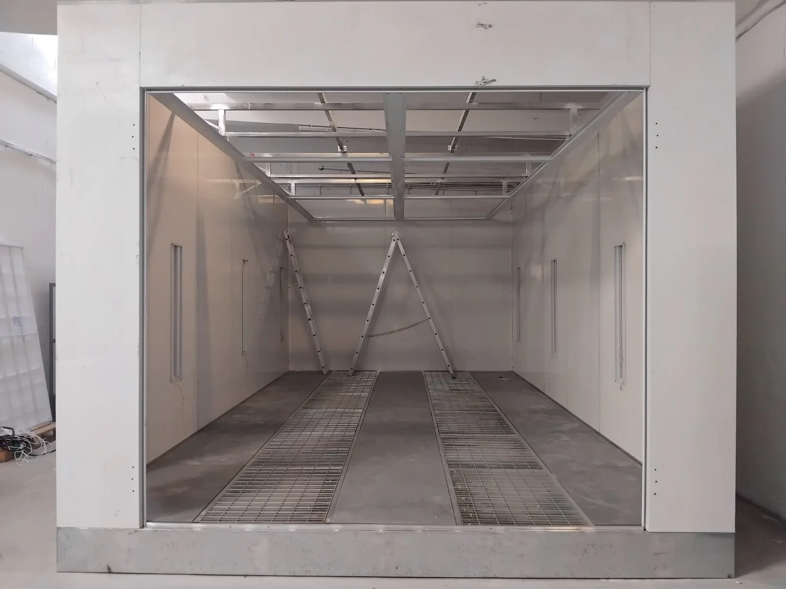 Leeres weißes Industrie-Schaltraum mit Metallgitterboden und zwei Klappleitern.