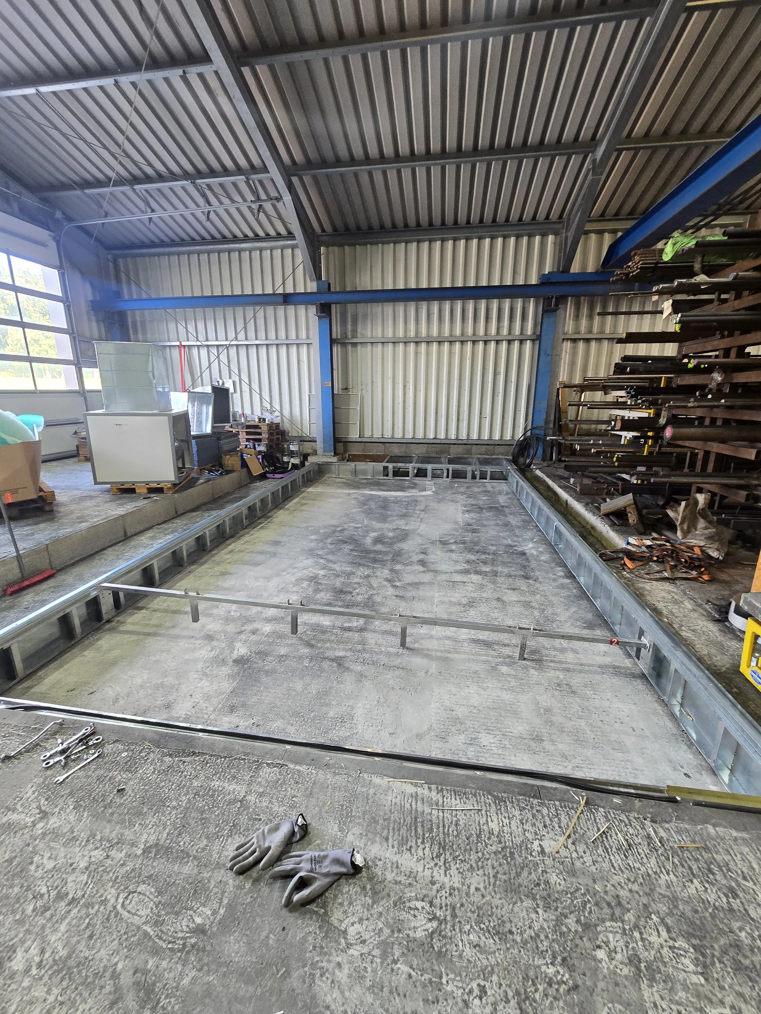 Bau eines Fundaments in einer Industriehalle, mit Sandbett und Metallrahmen, Werkzeug und Schutzhandschuhe im Vordergrund