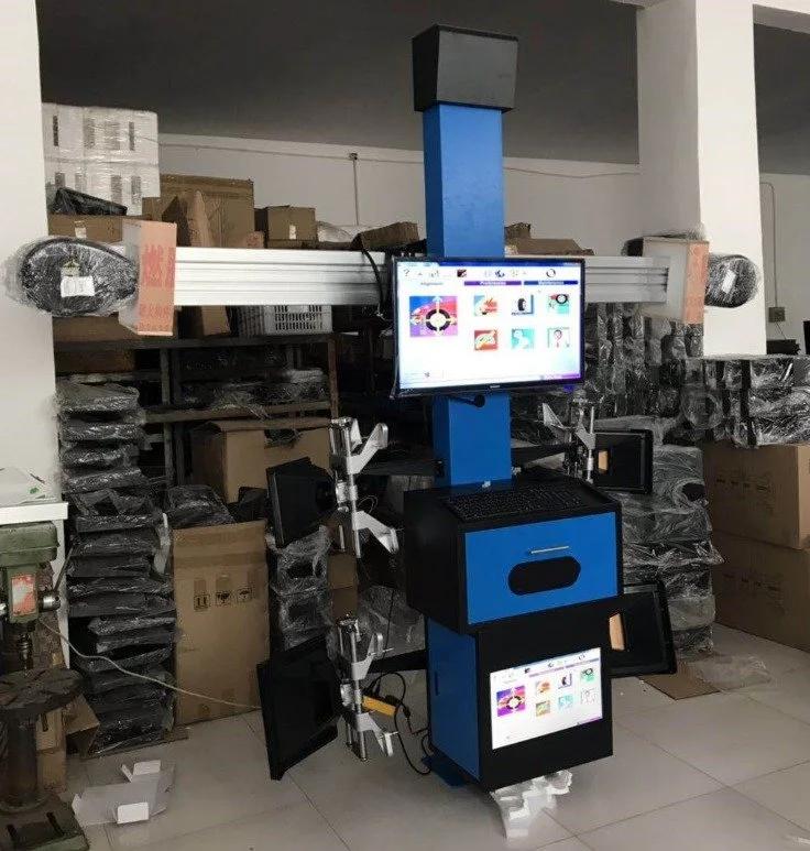 Ein technische Gerät mit zwei Bildschirmen, einem blauen Rahmen und mehreren Komponenten, in einem Lagerraum mit Kartons und Verpackungsmaterialien im Hintergrund.