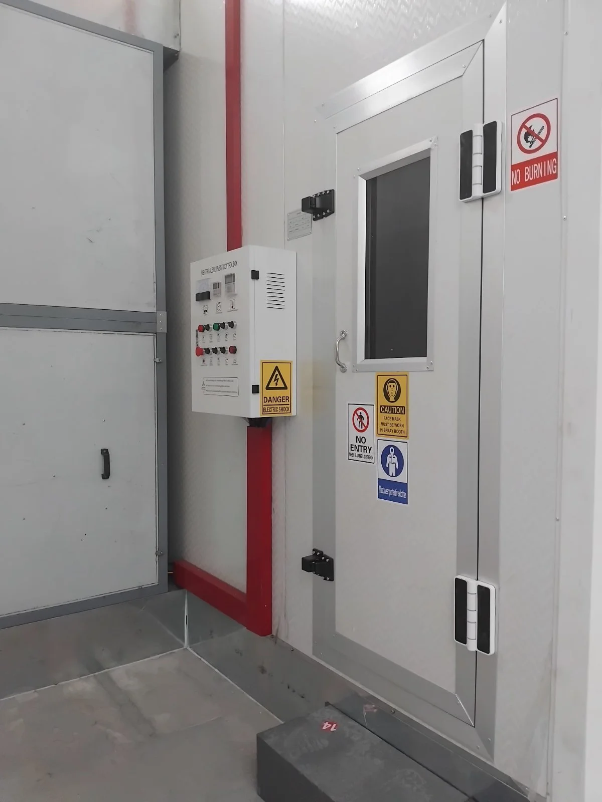 Sicherheits- und Warnschilder an einer Industrie-Tür, darunter Warnhinweise wie 'Kein Betreten', 'Gefahr elektrische Ladung', 'Vorschriften zum Tragen von Schutzhelmen', und eine Kontrolltafel an der Tür.