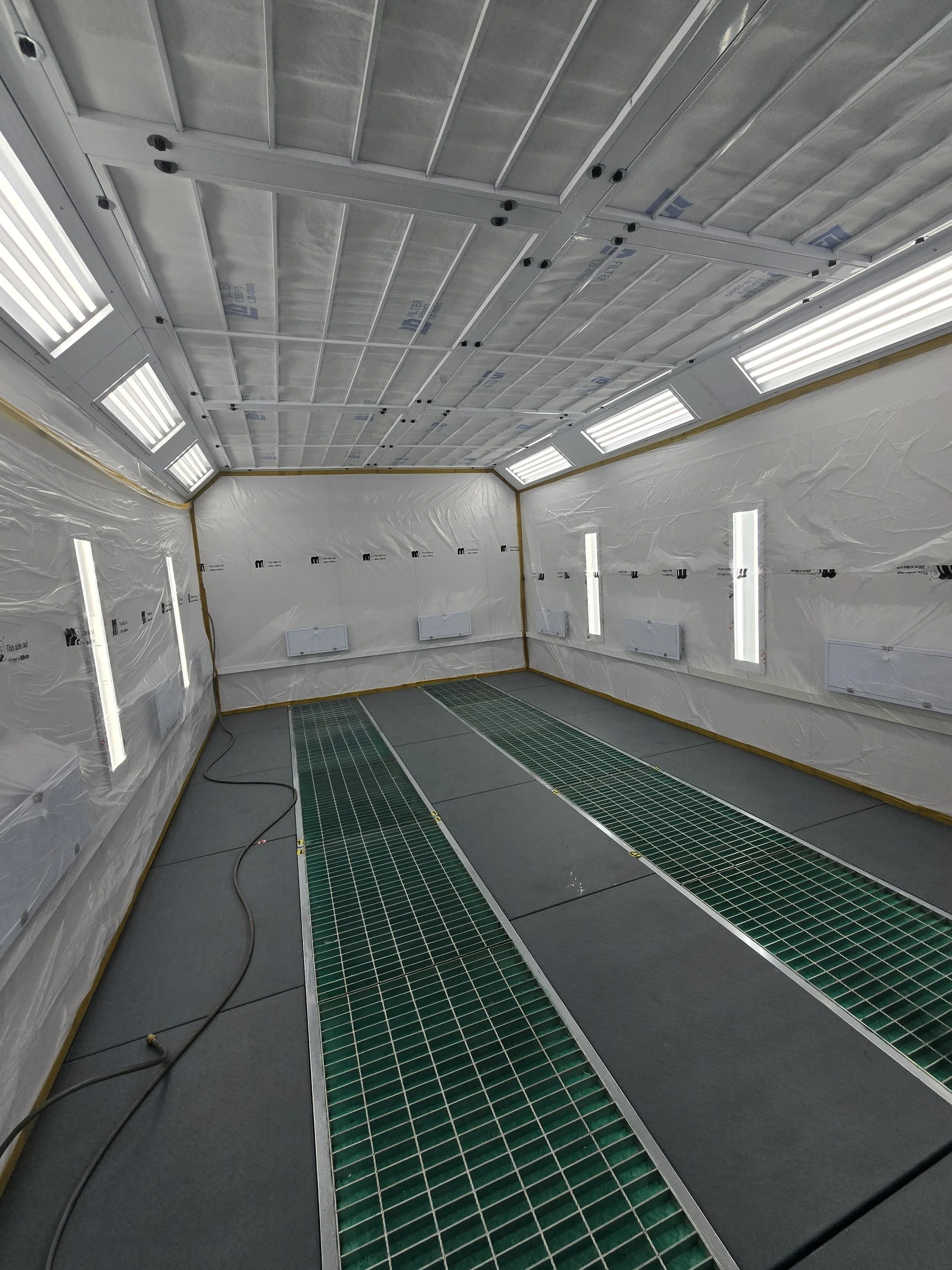 Ein Raum im Bau mit weißen Folien an den Wänden, einer Gitterwerk-Bodenabdeckung und einigen leuchtenden Leuchtstofflampen an der Decke.