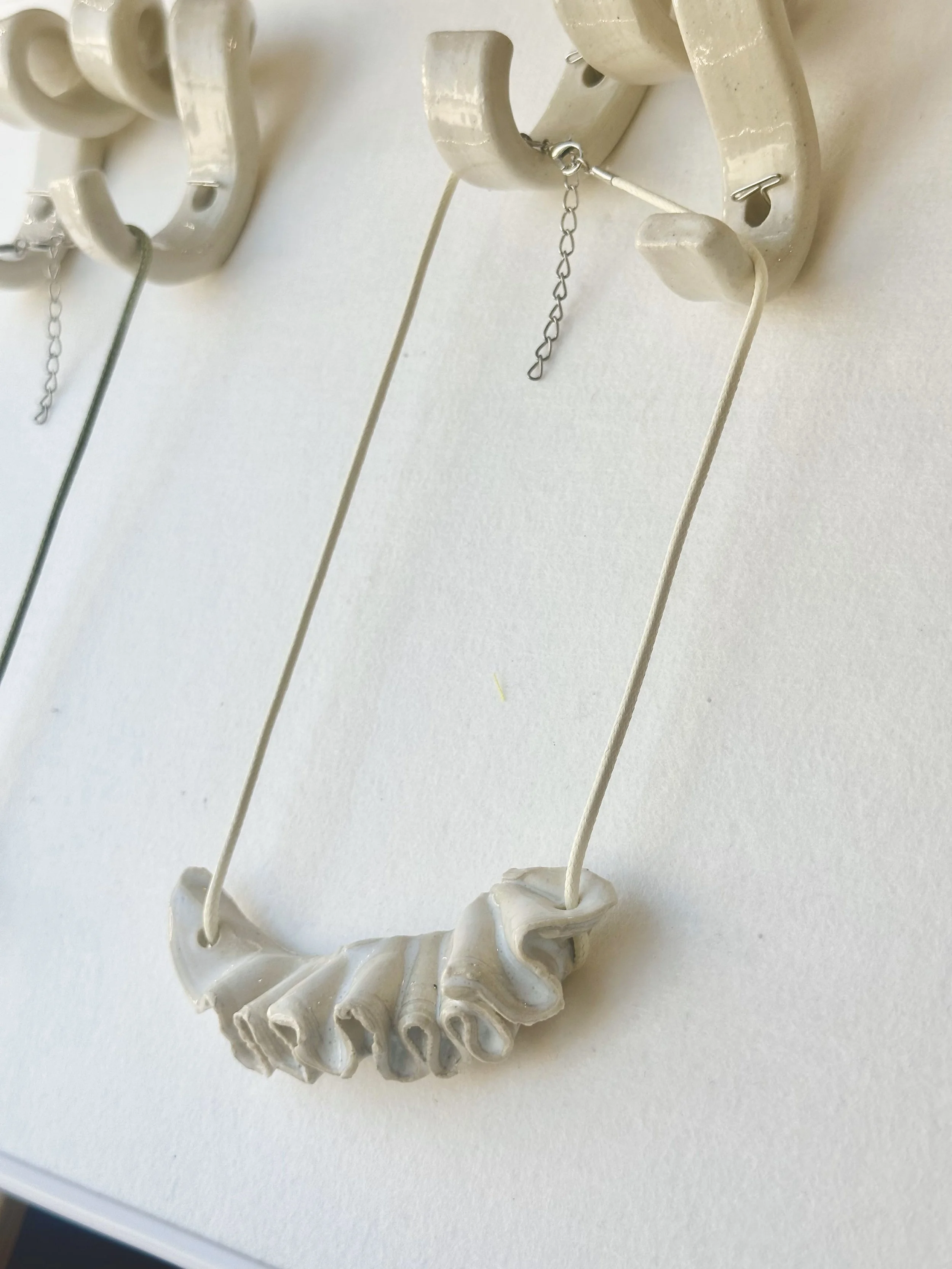Necklace with a ruffled ceramic pendant hanging on a white wall hook.