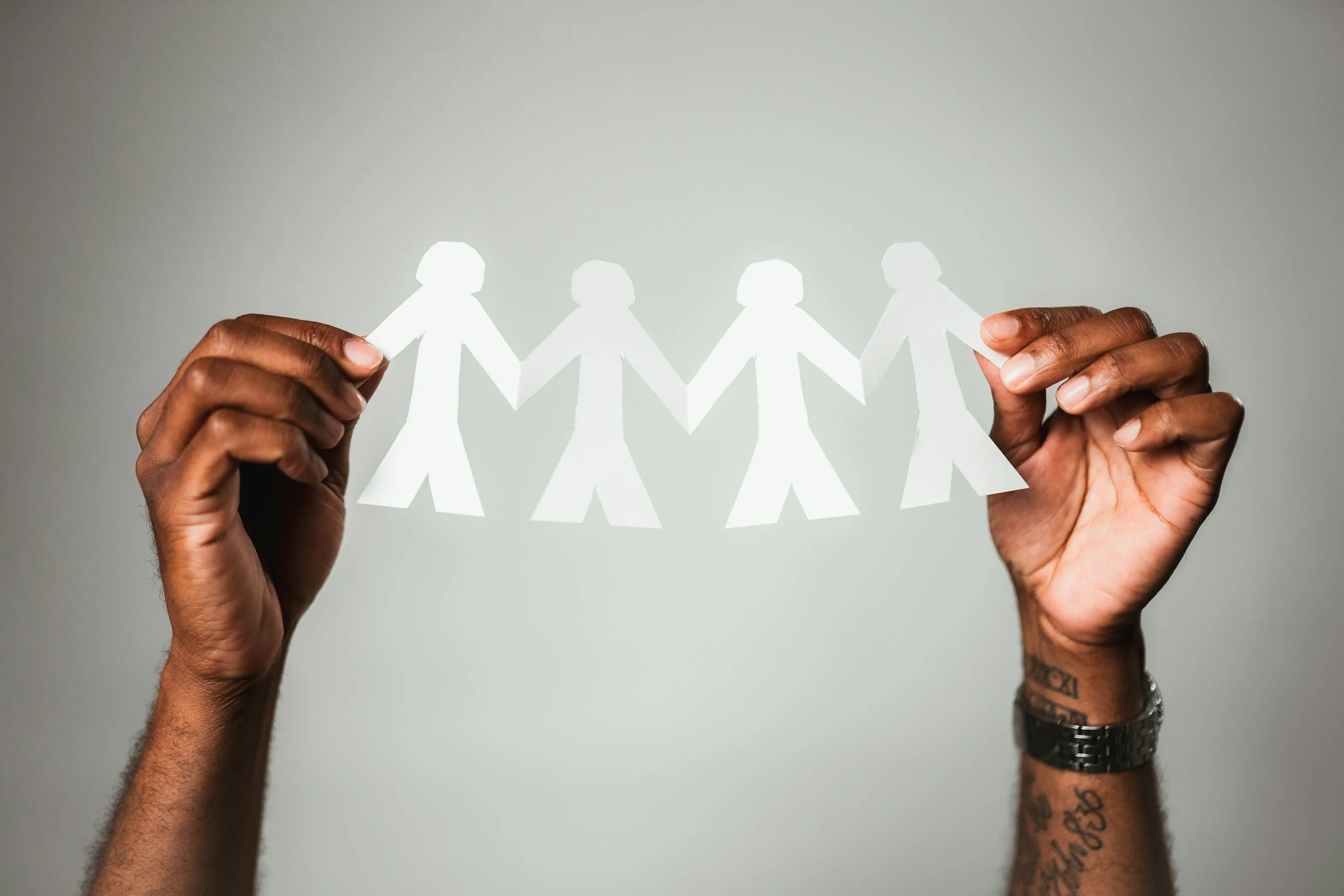 Hands holding paper cut-out figures linked together representing community healing and social connection in therapy