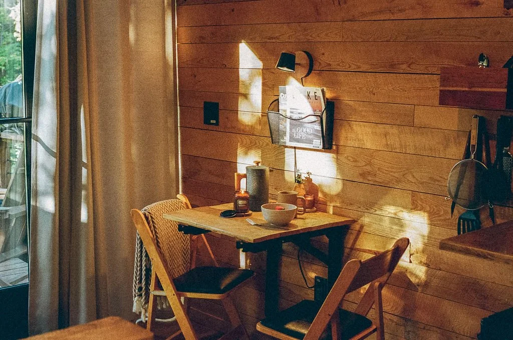 Cozy wooden dining nook with small table, two folding chairs, bowl, candle, and magazine rack on wall.