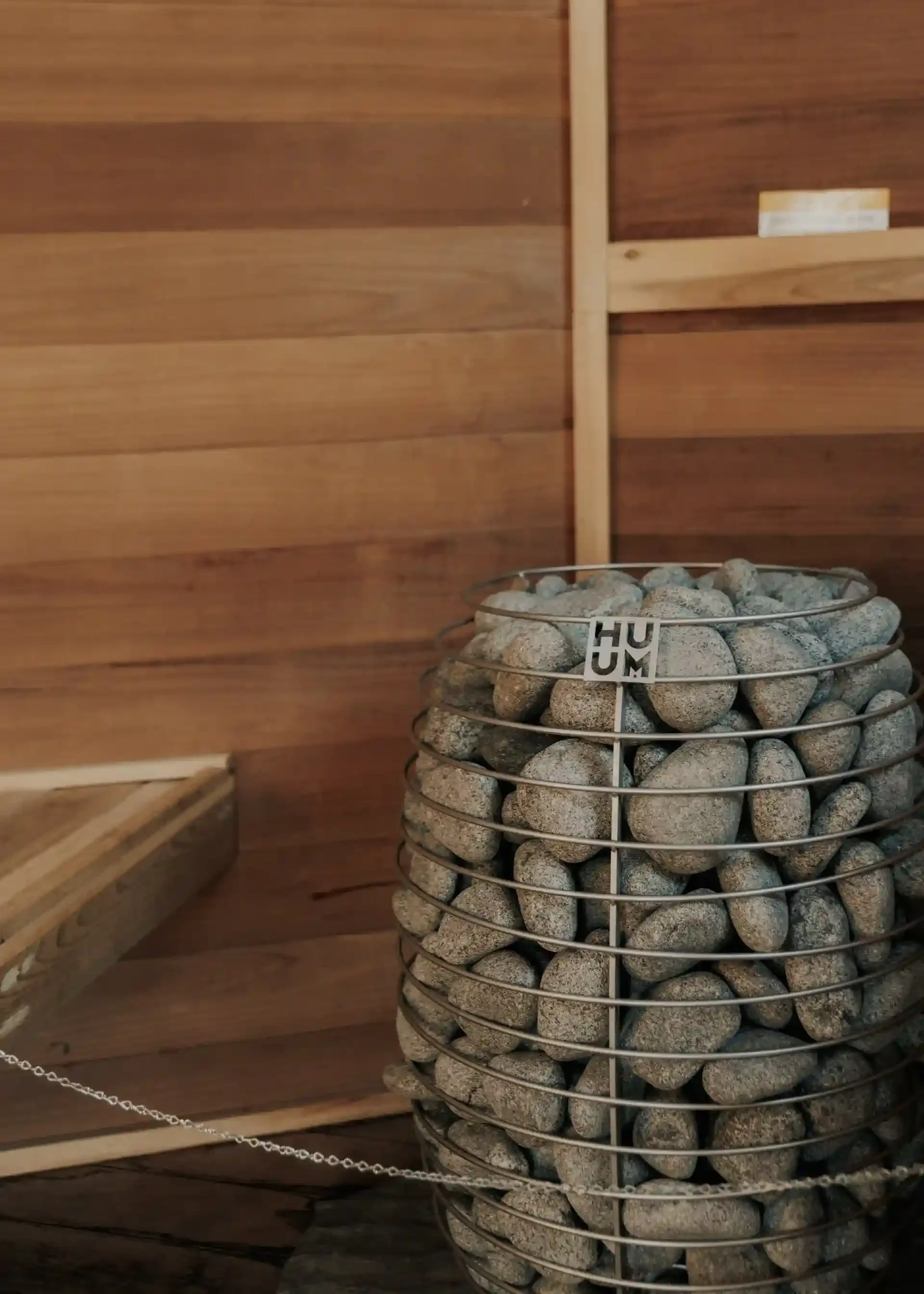 Metal basket filled with sauna stones inside a wooden sauna room.