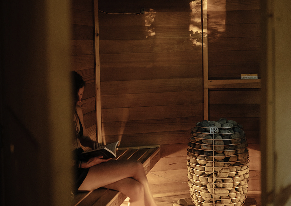 Interior of a wooden sauna with benches and a central heater surrounded by stones.