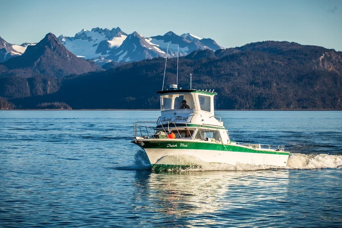 The Irish Mist fishing charter cruising through Kachemak Bay near Homer, Alaska, with snowcapped mountains and coastal scenery in the background on the Kenai Peninsula.