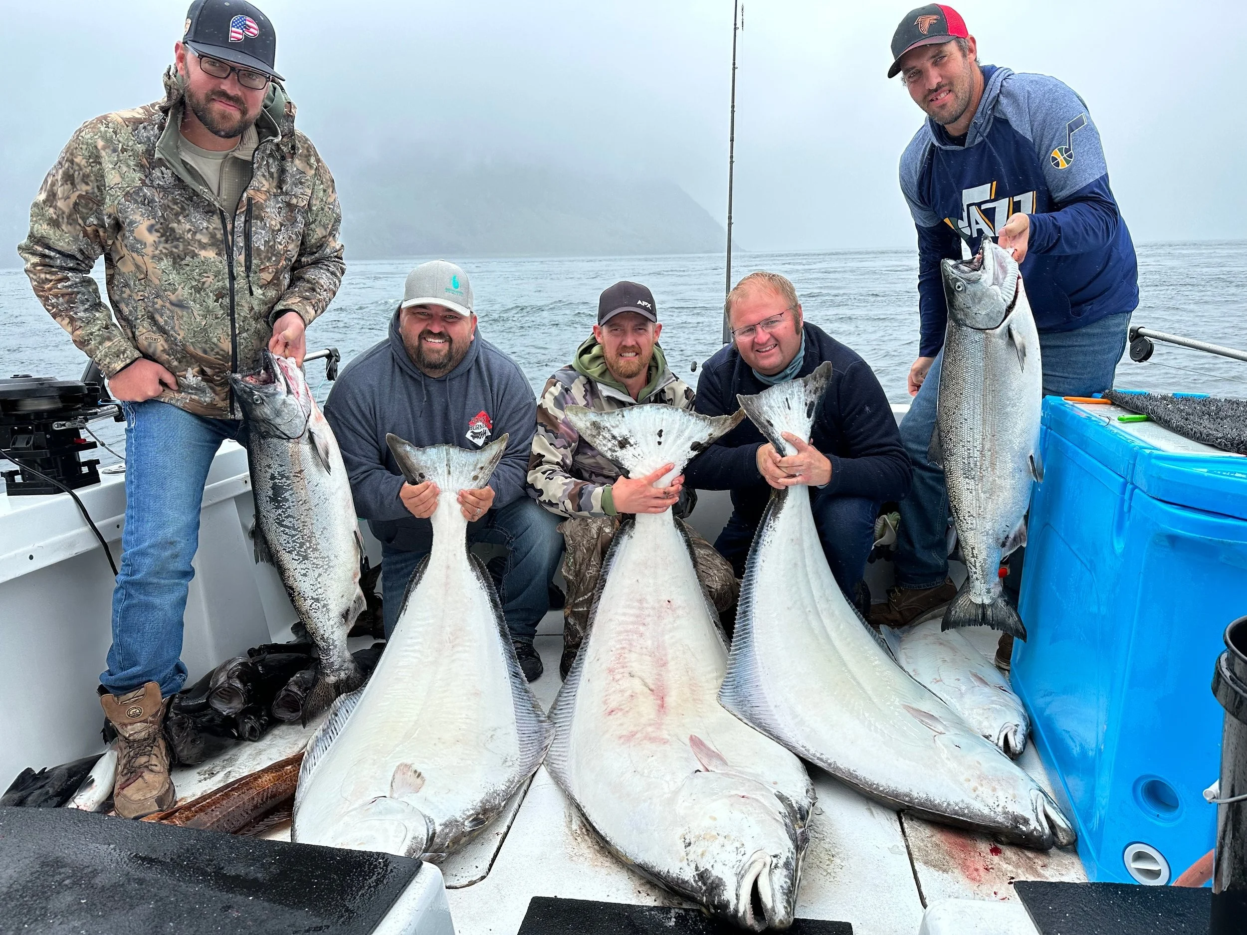 Group of anglers aboard a fishing charter in Kachemak Bay near Homer, Alaska, holding large halibut and salmon during a full-day Alaska fishing tour on the Kenai Peninsula.