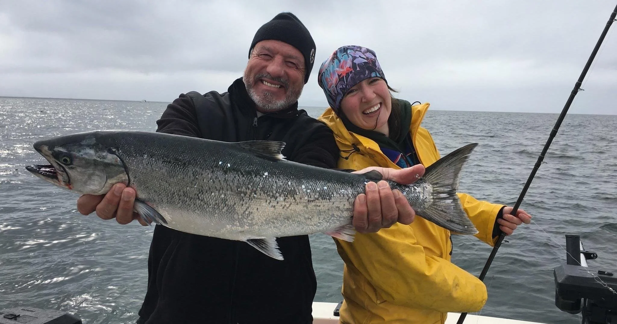 Two anglers holding a freshly caught salmon aboard a fishing boat in Kachemak Bay near Homer, Alaska, showcasing a successful saltwater fishing charter on the Kenai Peninsula.