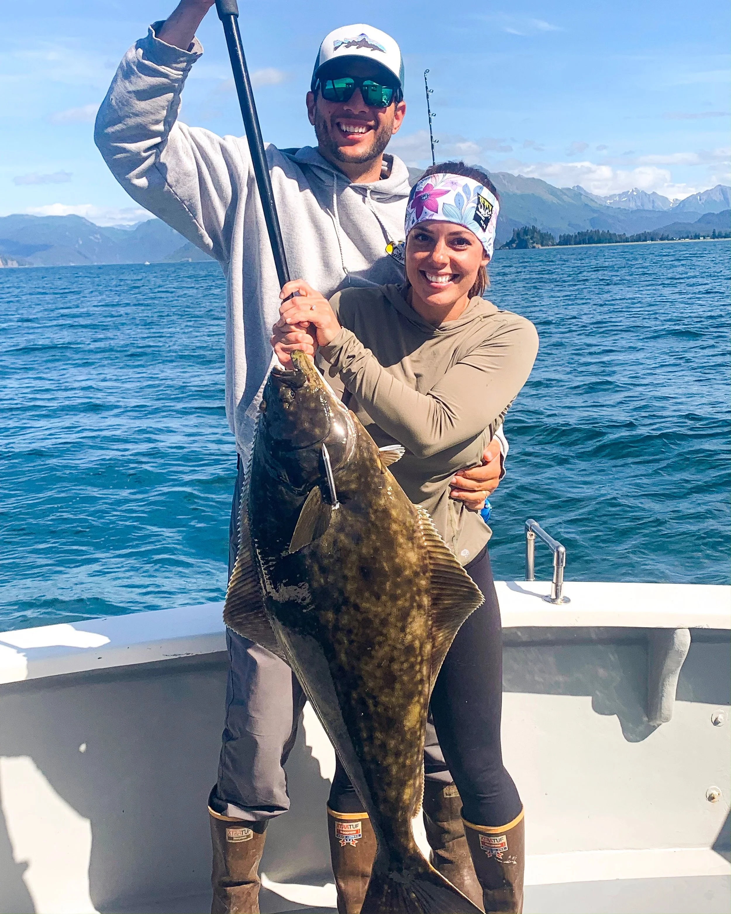 Couple halibut fishing in Homer, Alaska holding a halibut up on a sunny day.
