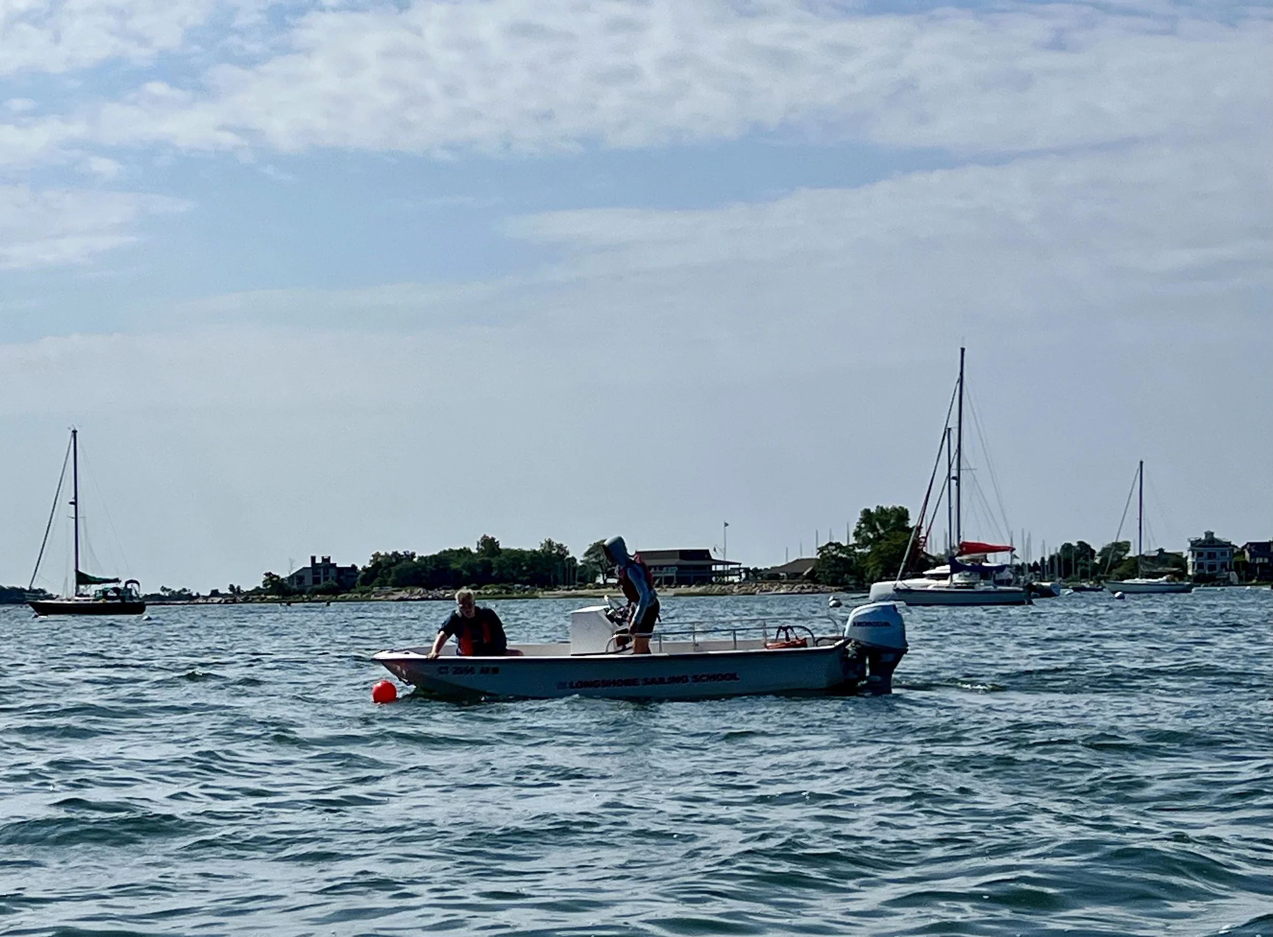 Two people in a small motorboat with sailboats in the background.