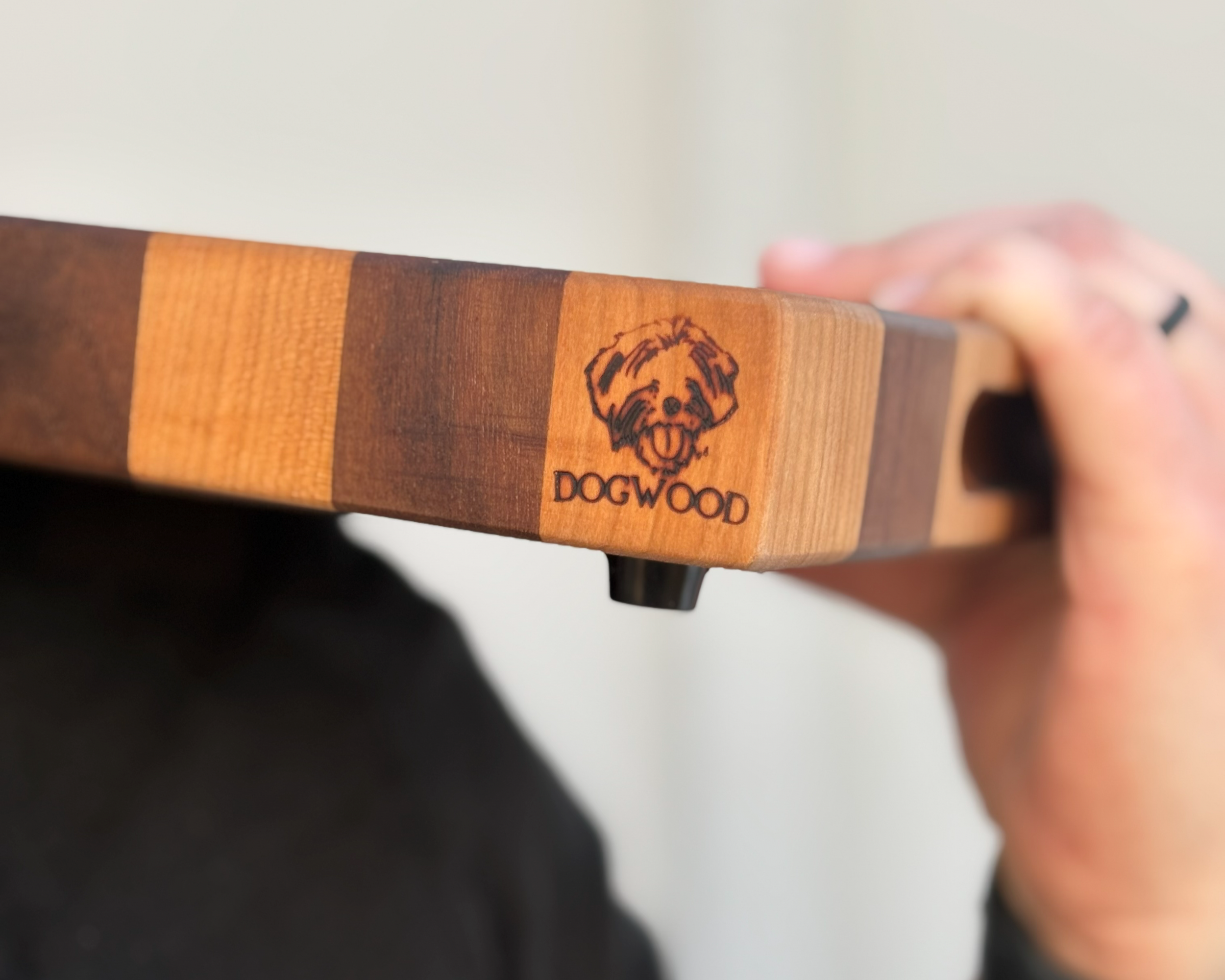 Close-up of a wooden object with a dog illustration and the text 'DOGWOOD', held by a person's hand.