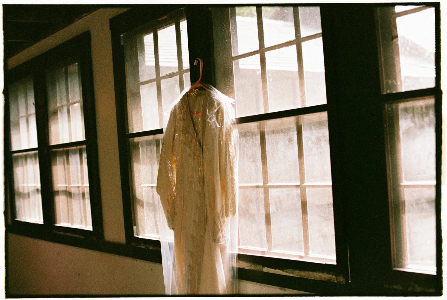 wedding gown hung up by large windows