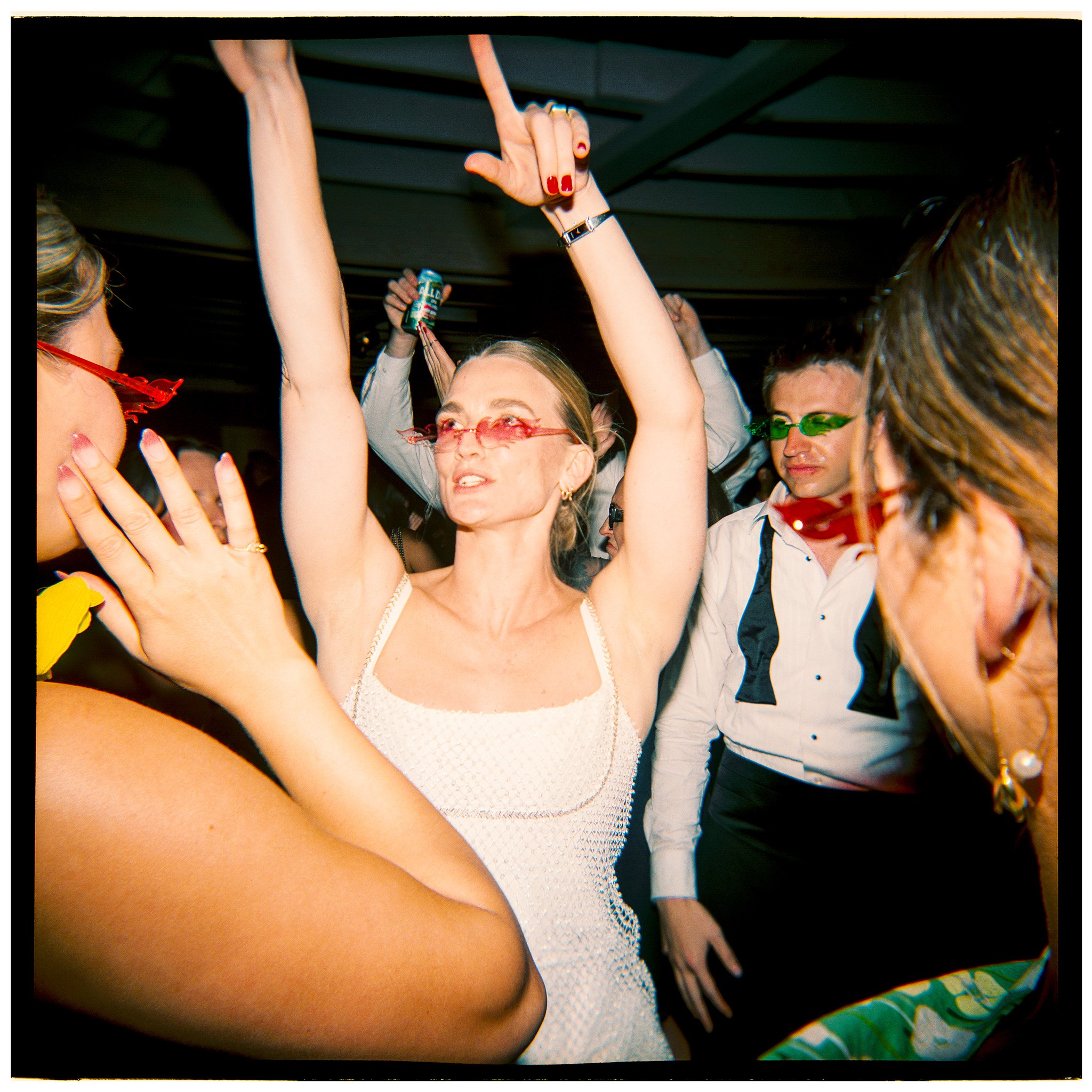 Group of people dancing and socializing at a party, with some wearing colorful sunglasses.