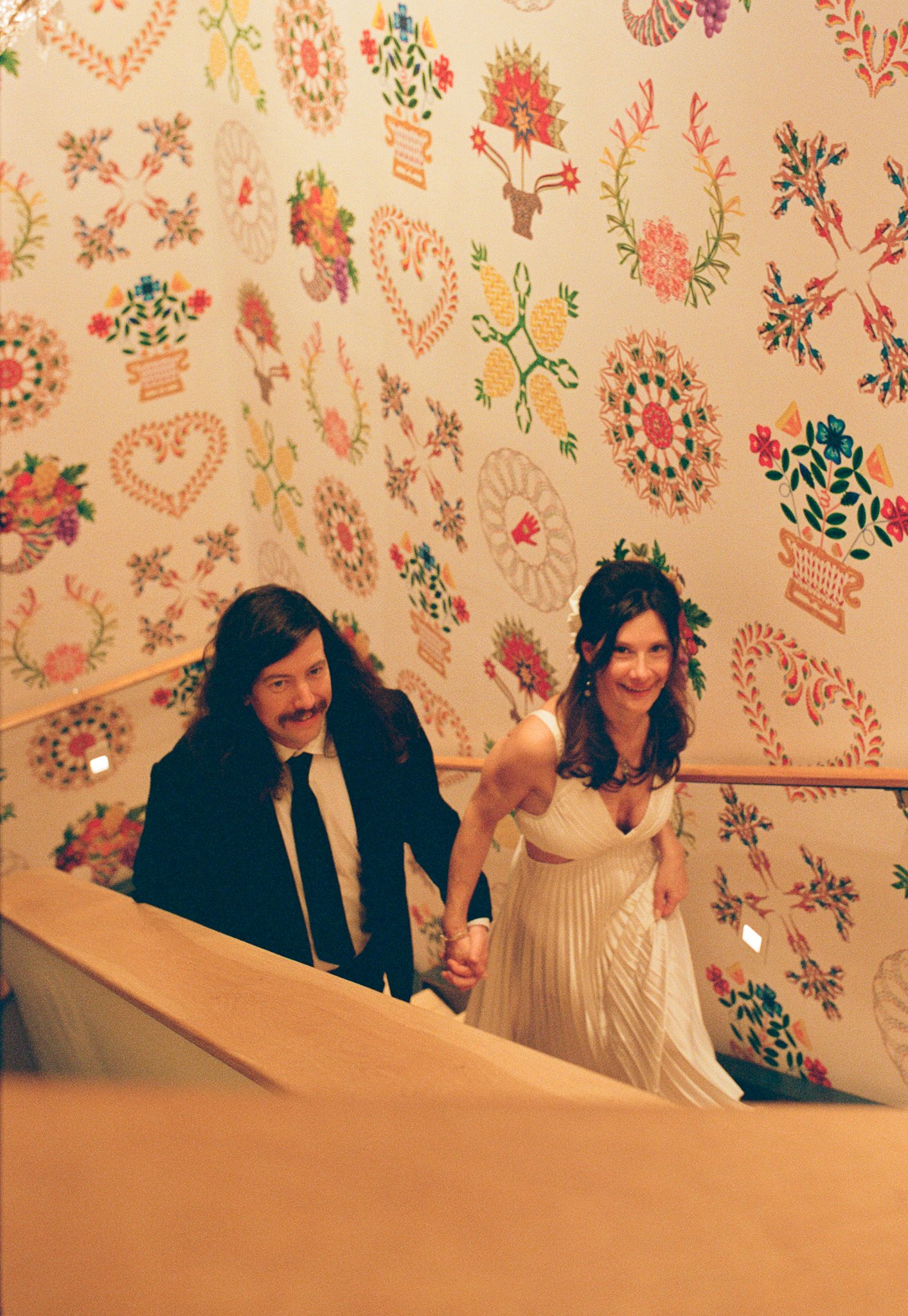 bride and groom walking up stairs with funky wallpaper behind them