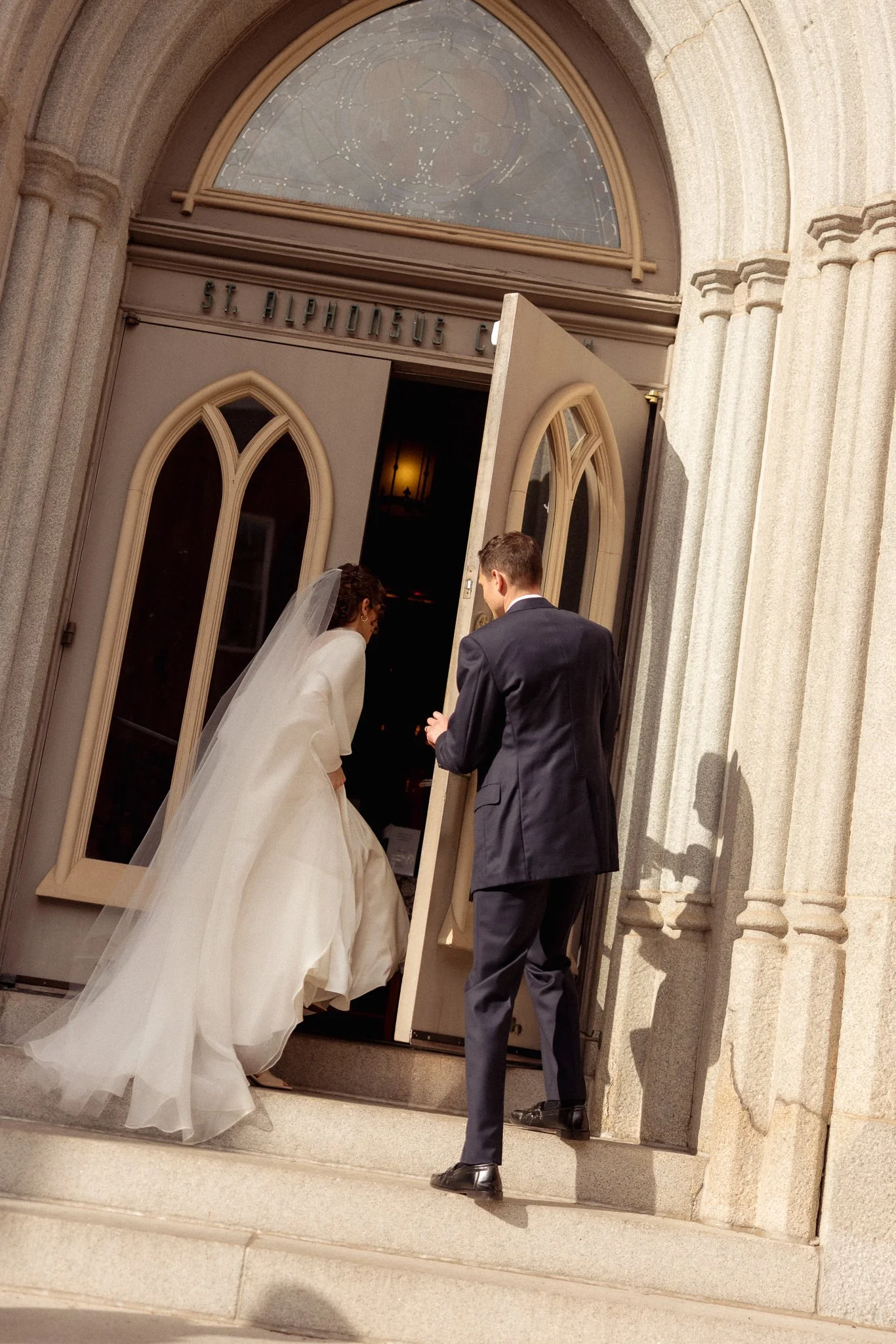 A bride and groom entering a church through open doors, with the church's name above the entrance.