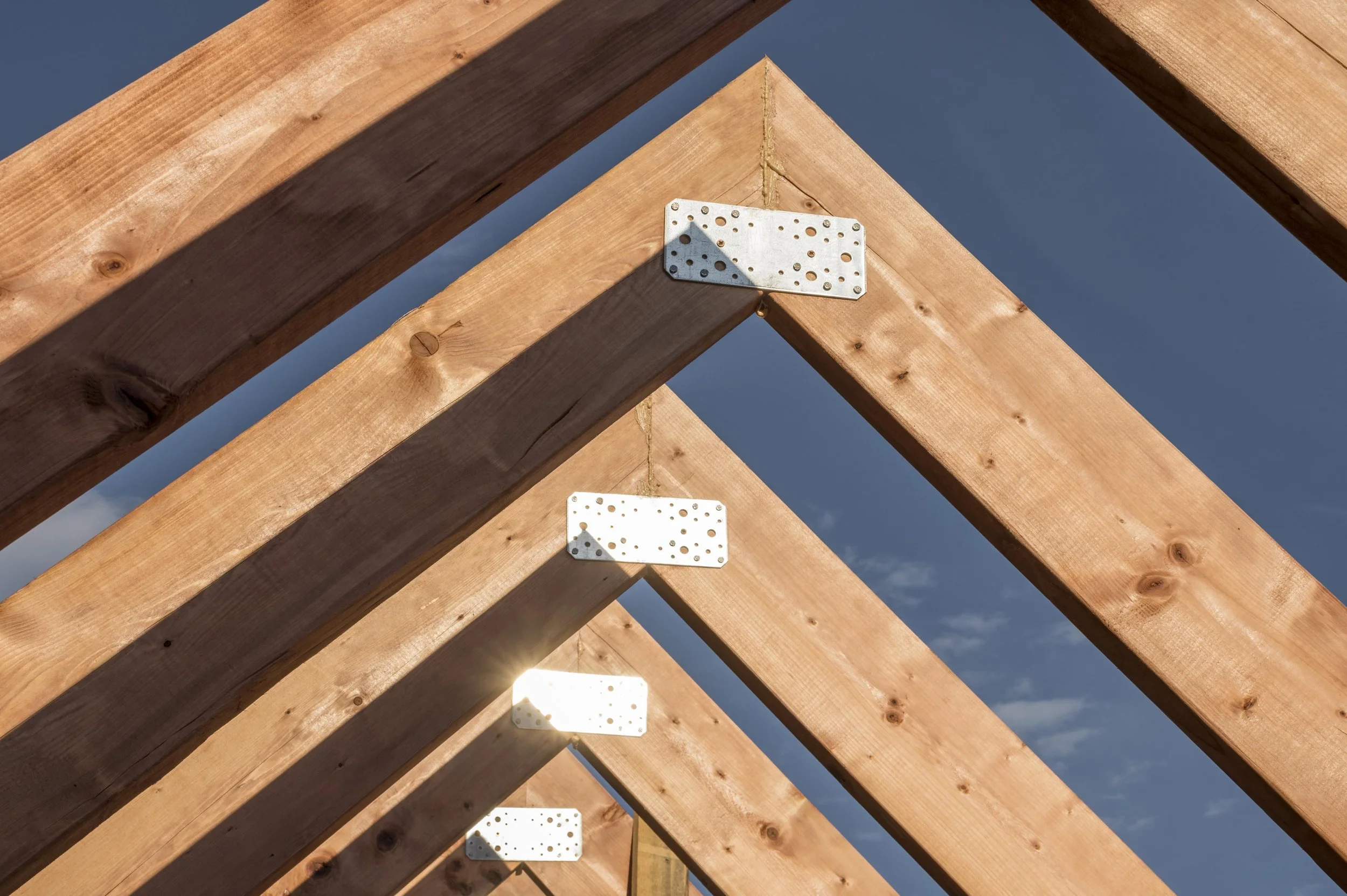 Wood roof trusses with metal connector plates forming a new home frame against a clear blue sky.