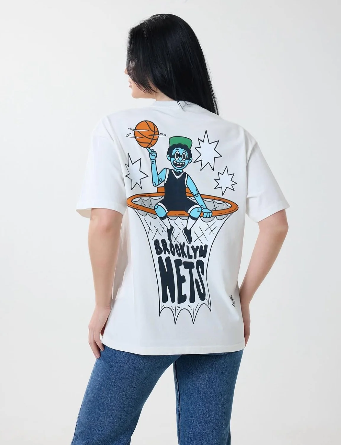 Person wearing a white Brooklyn Nets basketball graphic T-shirt with a cartoon boy playing basketball sitting on a hoop.