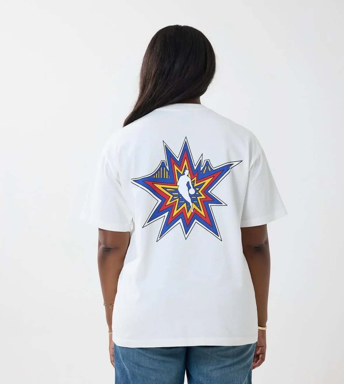 Person wearing a white T-shirt with a colorful graphic design of a starburst and a stylized figure on the back.