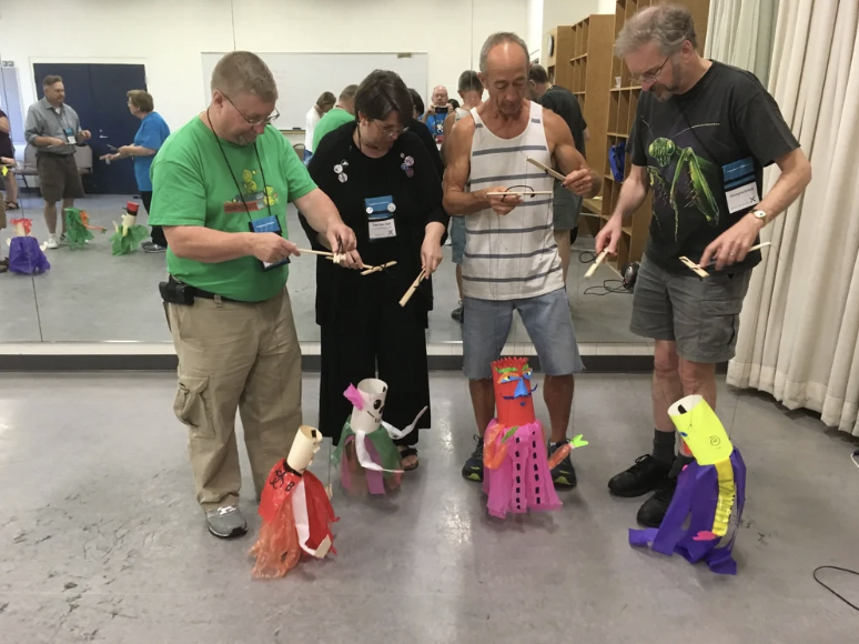A performer on stage wearing all black manipulates a marionette puppet that is wearing a floor length dress
