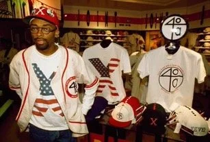 Man shopping in a store with clothing featuring American flag and 4/20 designs, surrounded by hats and shirts with similar themes.
