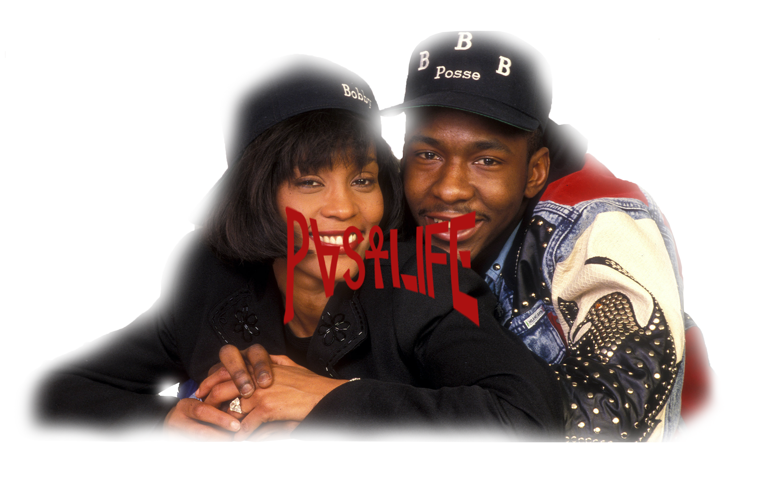 A smiling woman and man closely leaning together, both wearing black hats and fashionable clothing. The woman has dark hair and the man is wearing a denim jacket with decorative elements.