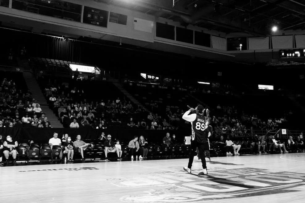 A basketball court with a player wearing jersey number 89, standing near a teammate, in front of a seated audience in an indoor arena.