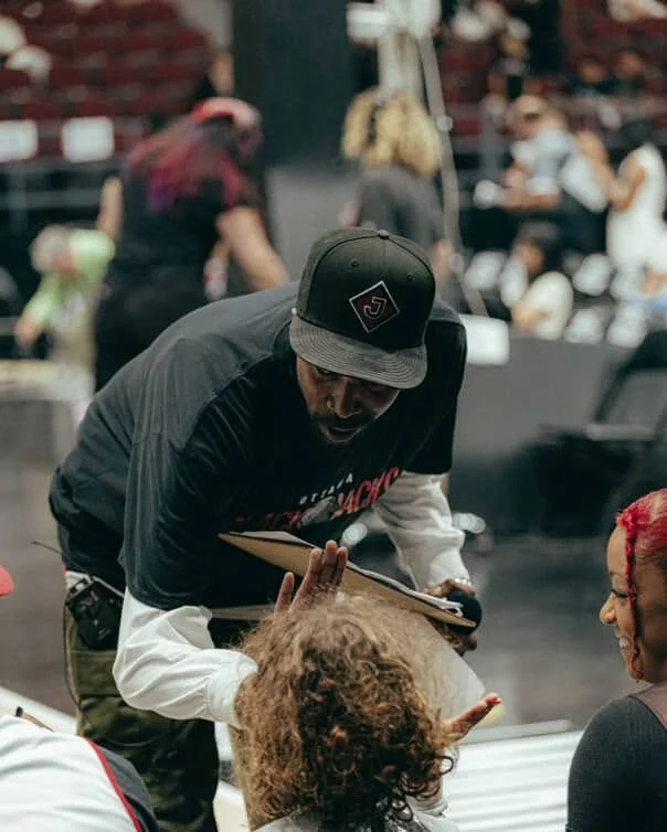 A man with a black cap and black T-shirt leaning over a group of women, involved in a discussion.