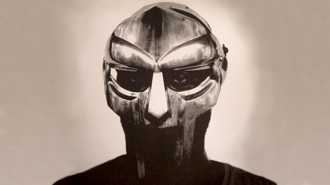 A metallic mask resembling a human face with sunglasses and a hooded garment, viewed in black and white.