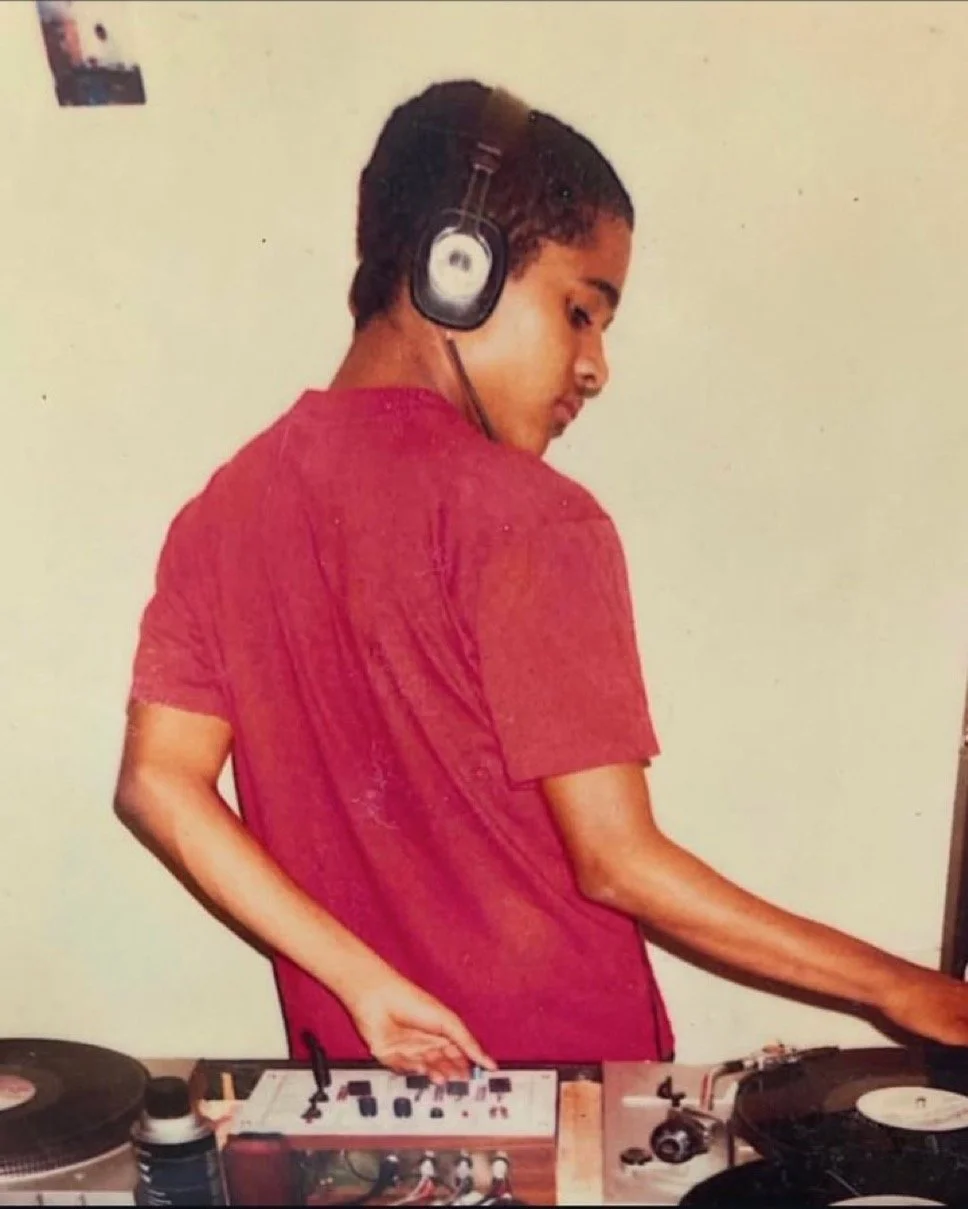 Young boy DJing with headphones, wearing a red shirt, standing behind a turntable and sound mixer.
