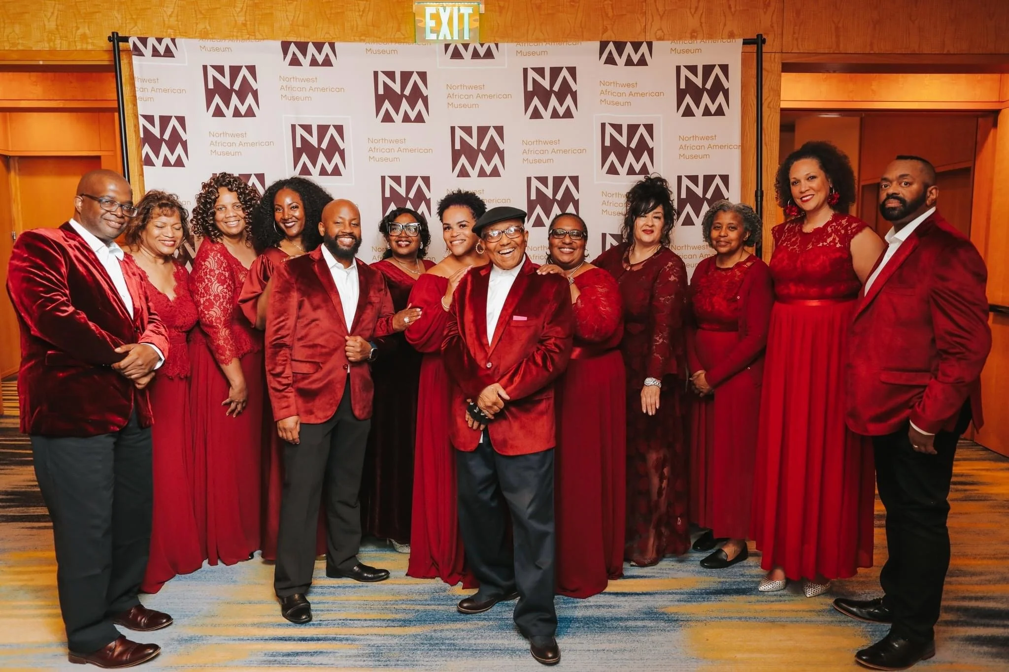 Group of people in red and black formal attire posing in front of a Northwest African American Museum backdrop.