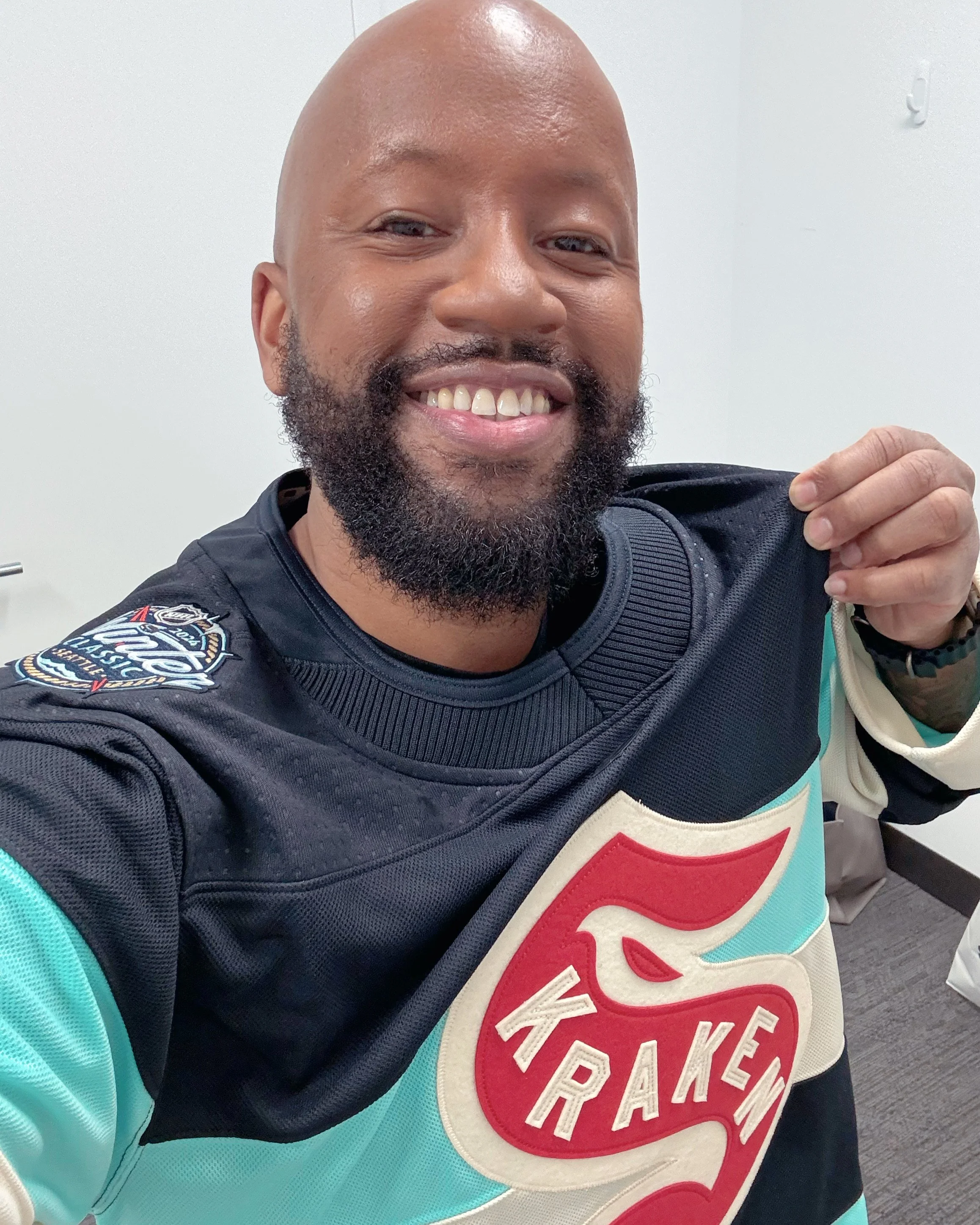 Person smiling and holding their Seattle Kraken jersey, featuring a prominent red Kraken logo on the front.
