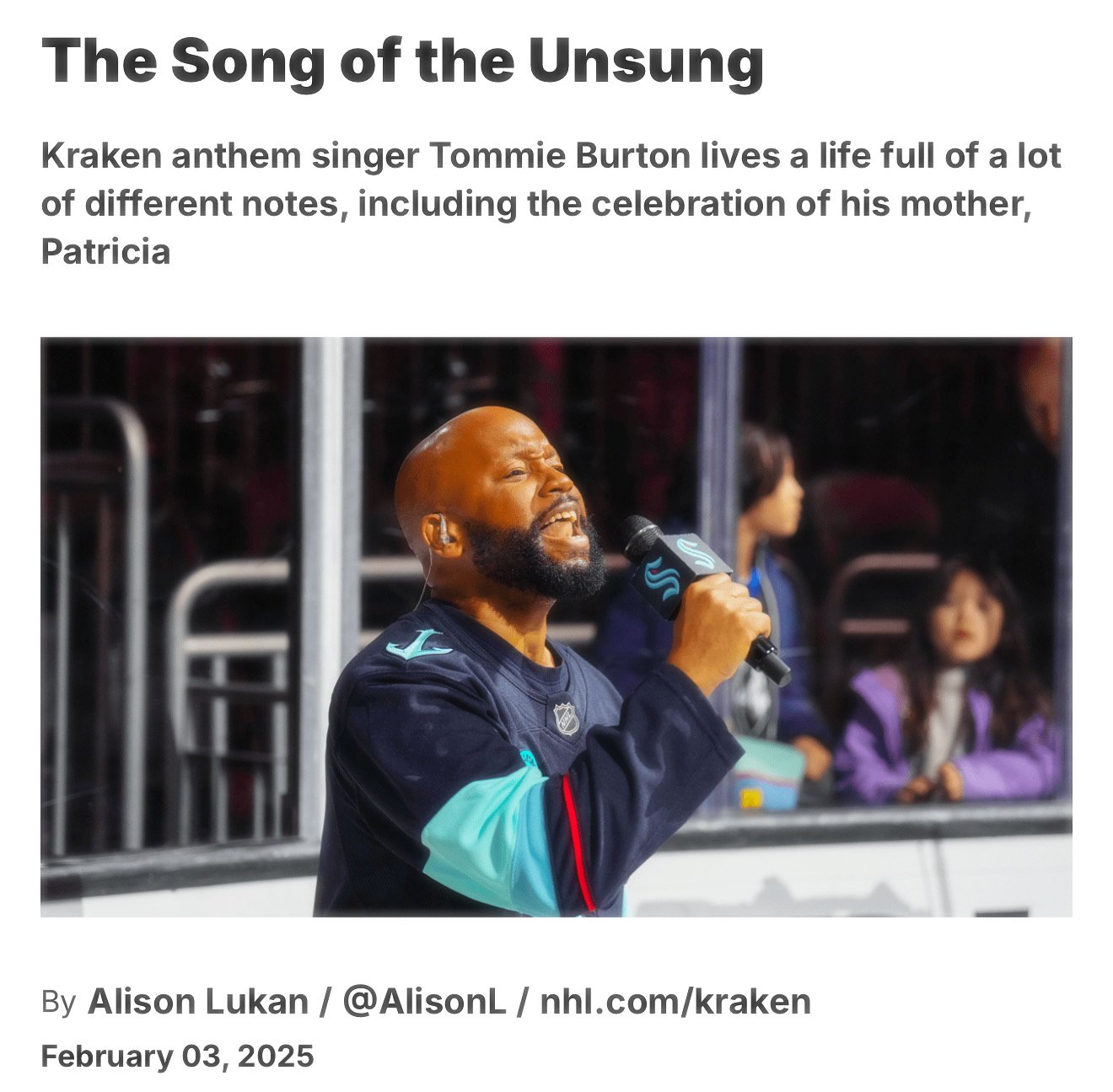 Person singing into a microphone at a sports venue, wearing a jersey with teal sleeves. Spectators are visible in the background.